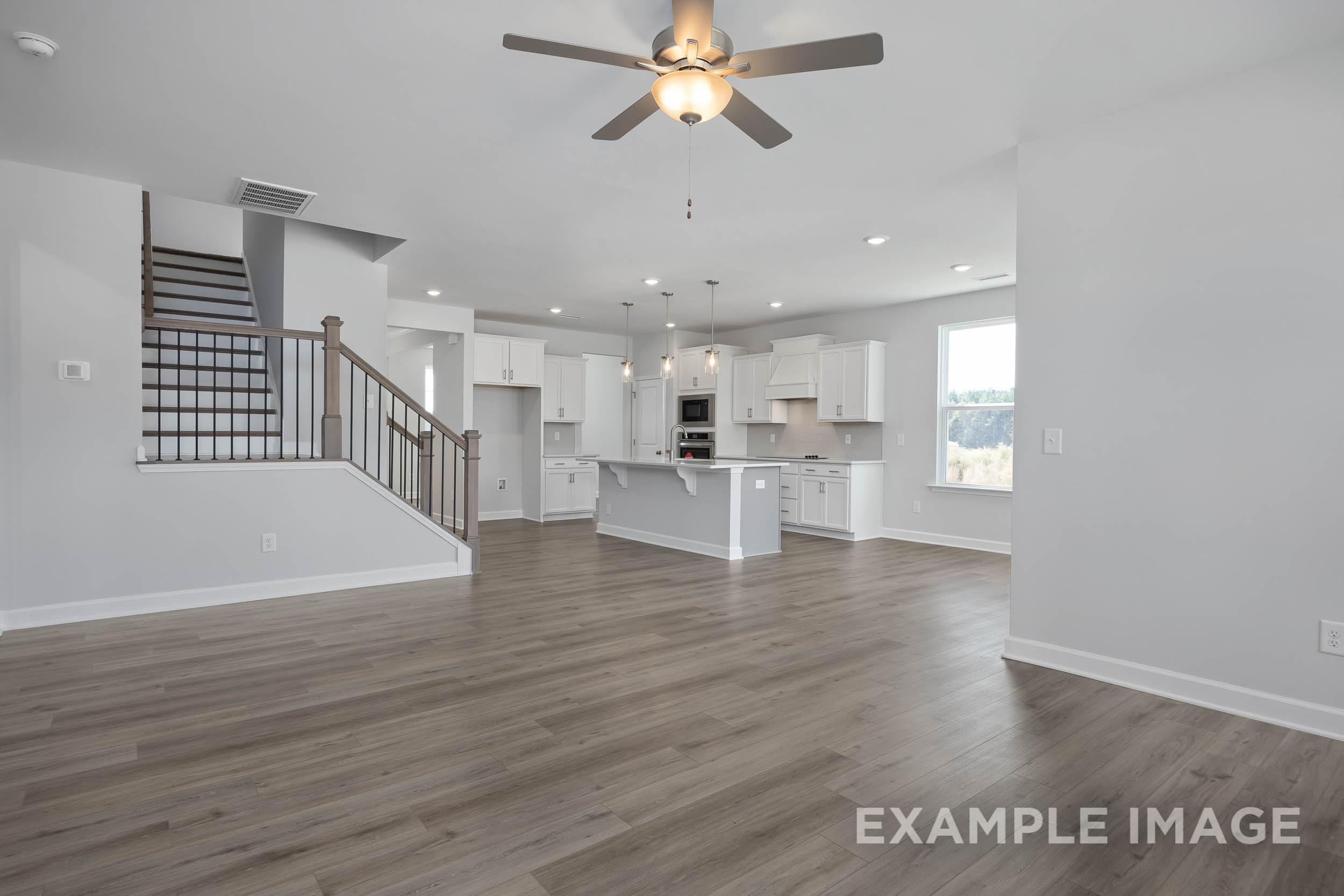 Spacious open-concept kitchen in The Ash home with white cabinets, large island, hardwood floors, and ceiling fan