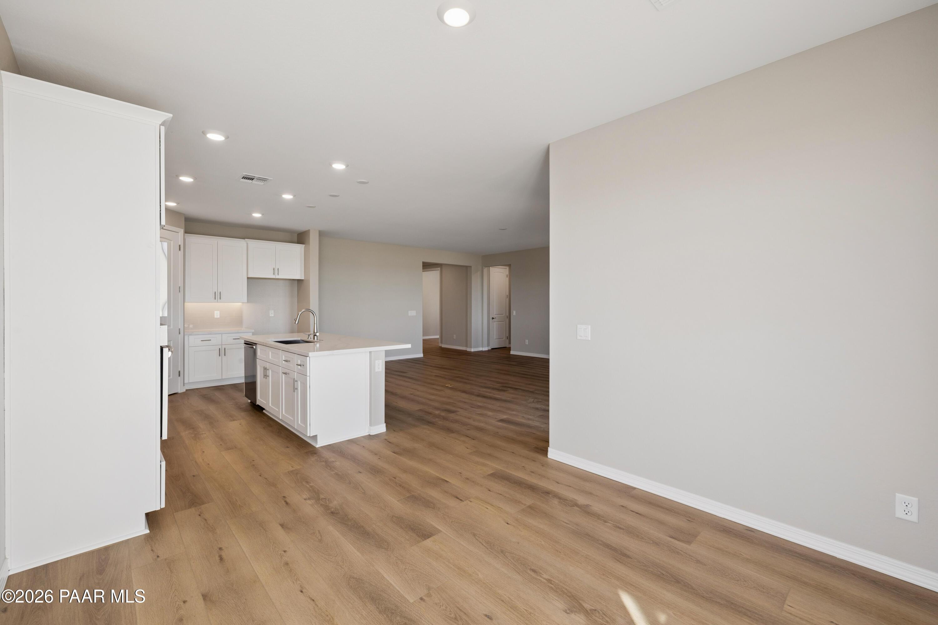 Modern open-concept kitchen with white cabinets, center island, stainless fridge, and hardwood floors in Davidson Homes The Harmony A, Prescott Valley, AZ