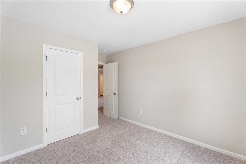 Neutral-toned empty bedroom with beige walls, carpet floor, white doors, and ceiling light in Evermore Homes The Washington, Phenix City, AL