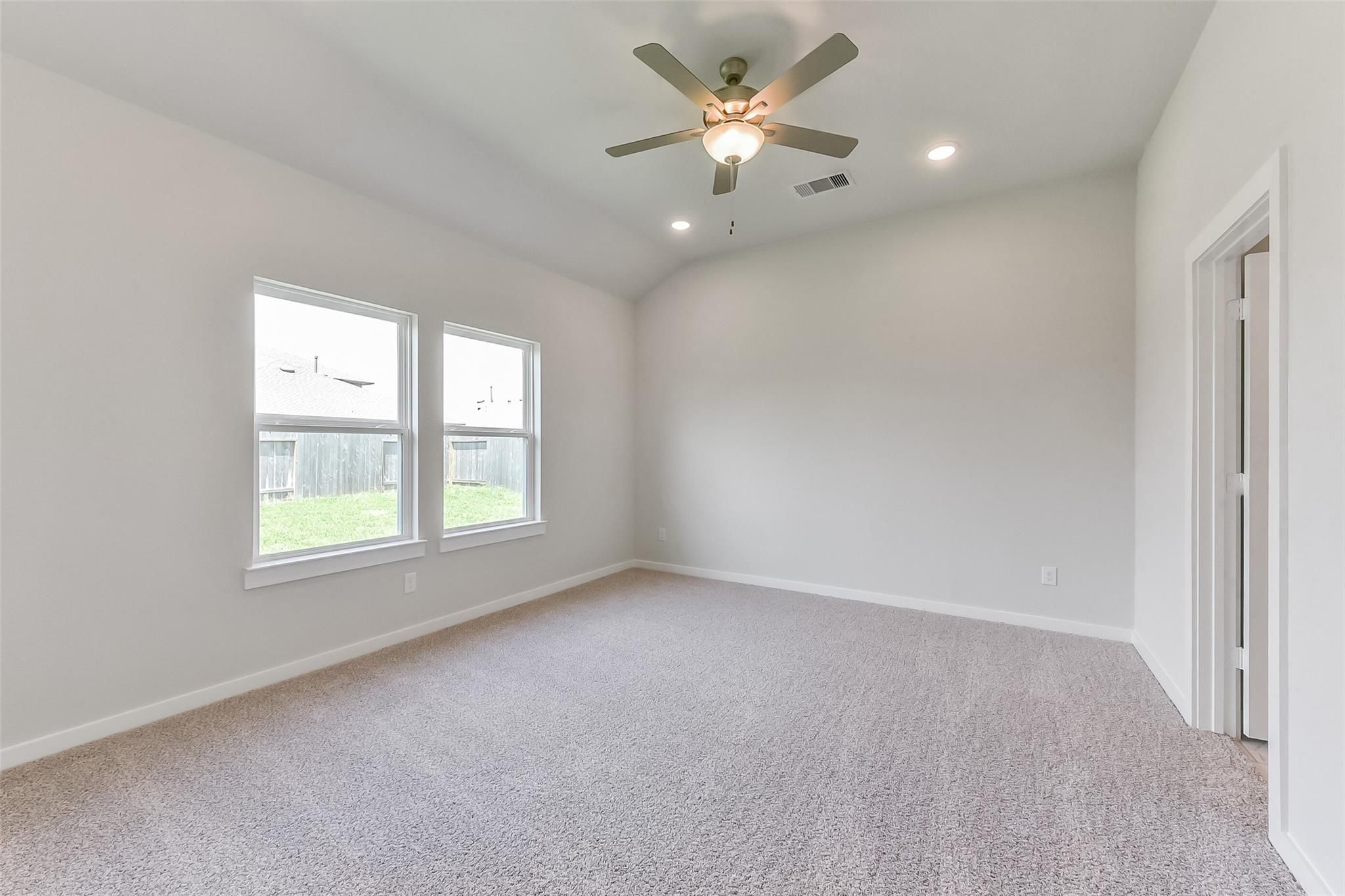 Spacious bedroom with neutral walls, plush carpet, ceiling fan, and backyard-view windows in Davidson Homes The Tierra C, Dayton, Texas