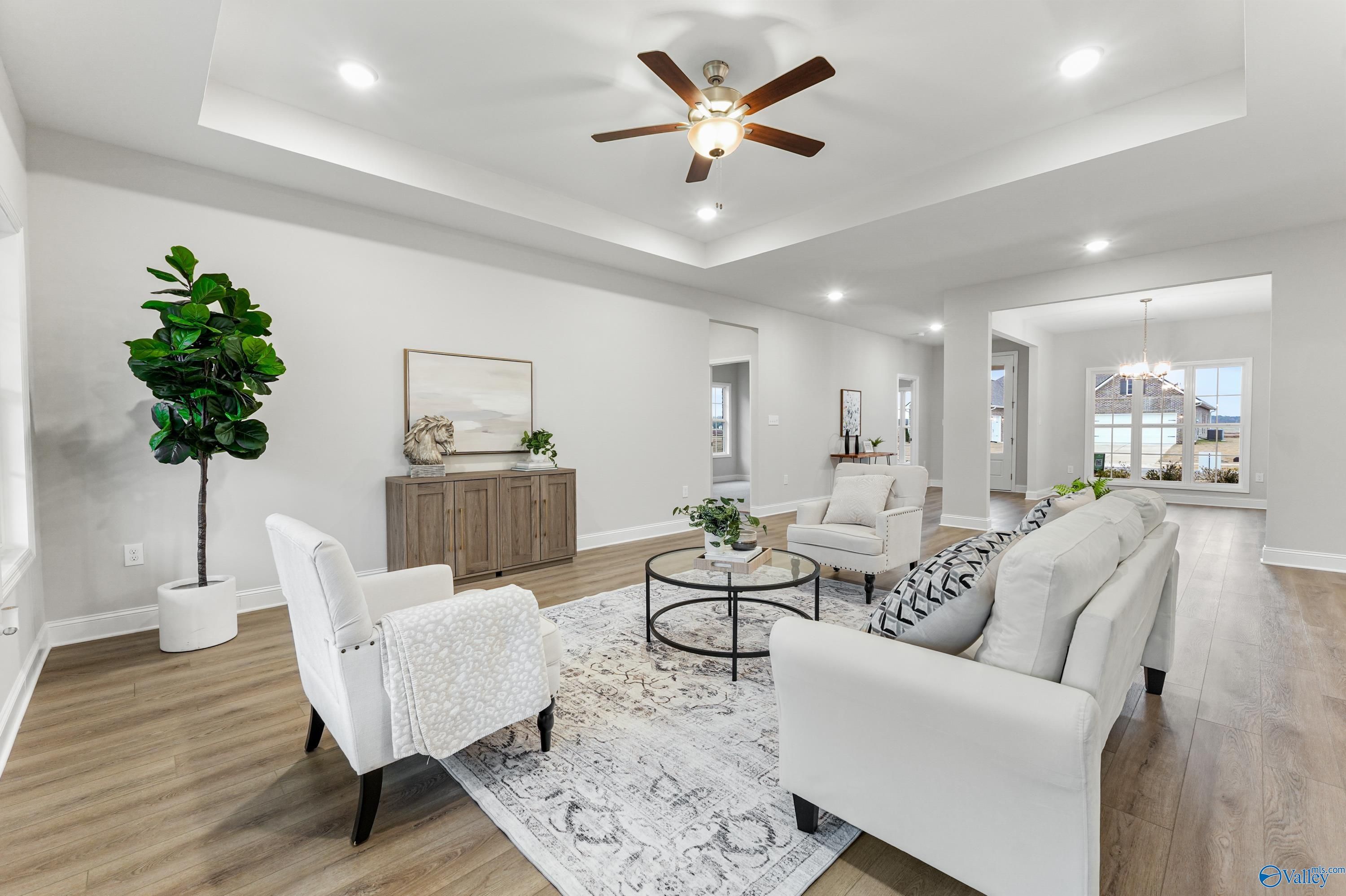 Bright open living room with white sofa, armchairs, ceiling fan, and fiddle leaf fig in Davidson Homes The Finleigh, Toney, Alabama