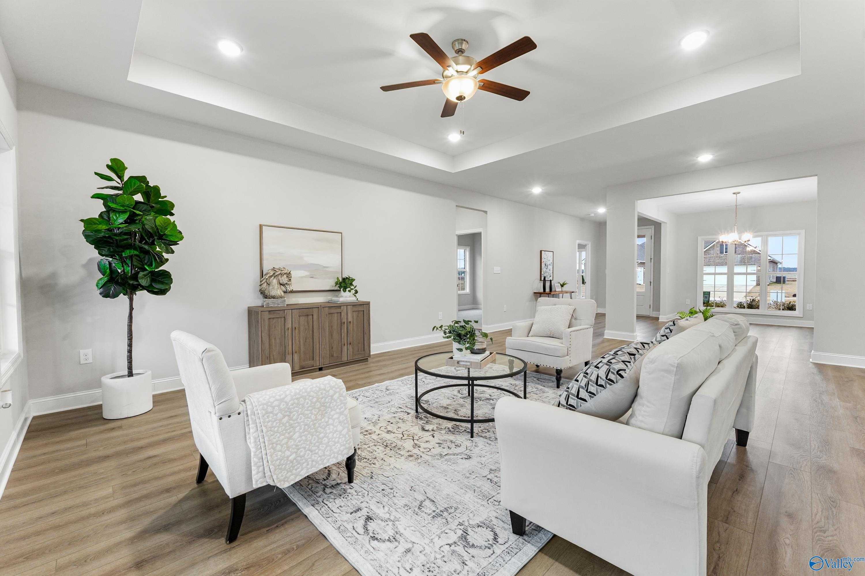 Bright open living room with white sofa, armchairs, ceiling fan, and fiddle leaf fig in Davidson Homes The Finleigh, Toney, Alabama