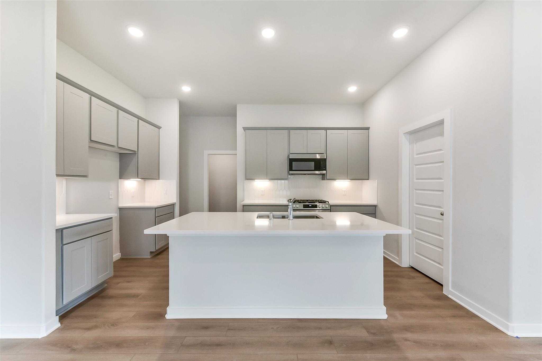 Modern kitchen with white quartz island, gray cabinets, stainless appliances in Davidson Homes The Laguna C, Rosharon, Texas