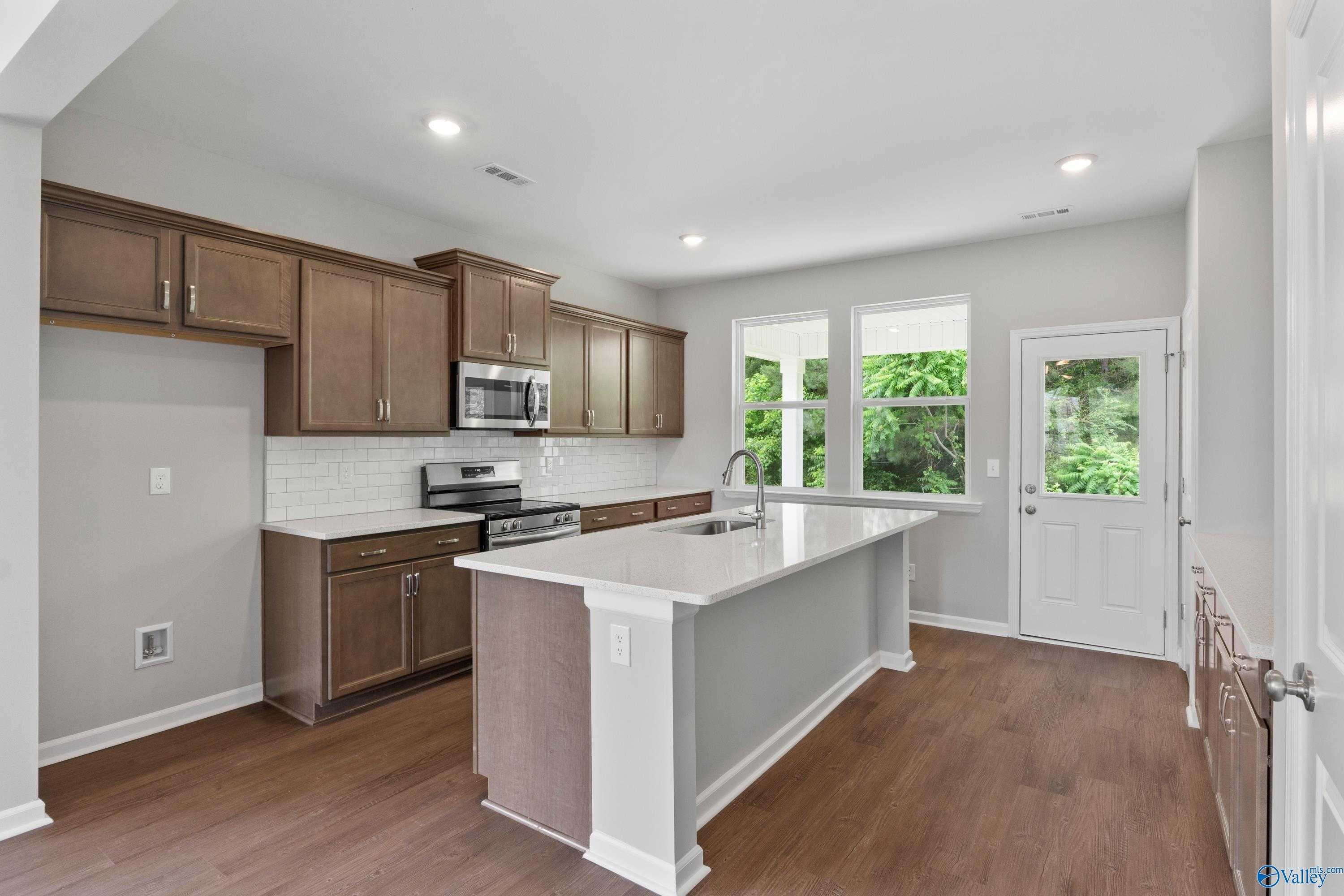 Contemporary kitchen with brown shaker cabinets, white quartz island, stainless appliances in The Stella by Davidson Homes, Hazel Green, AL