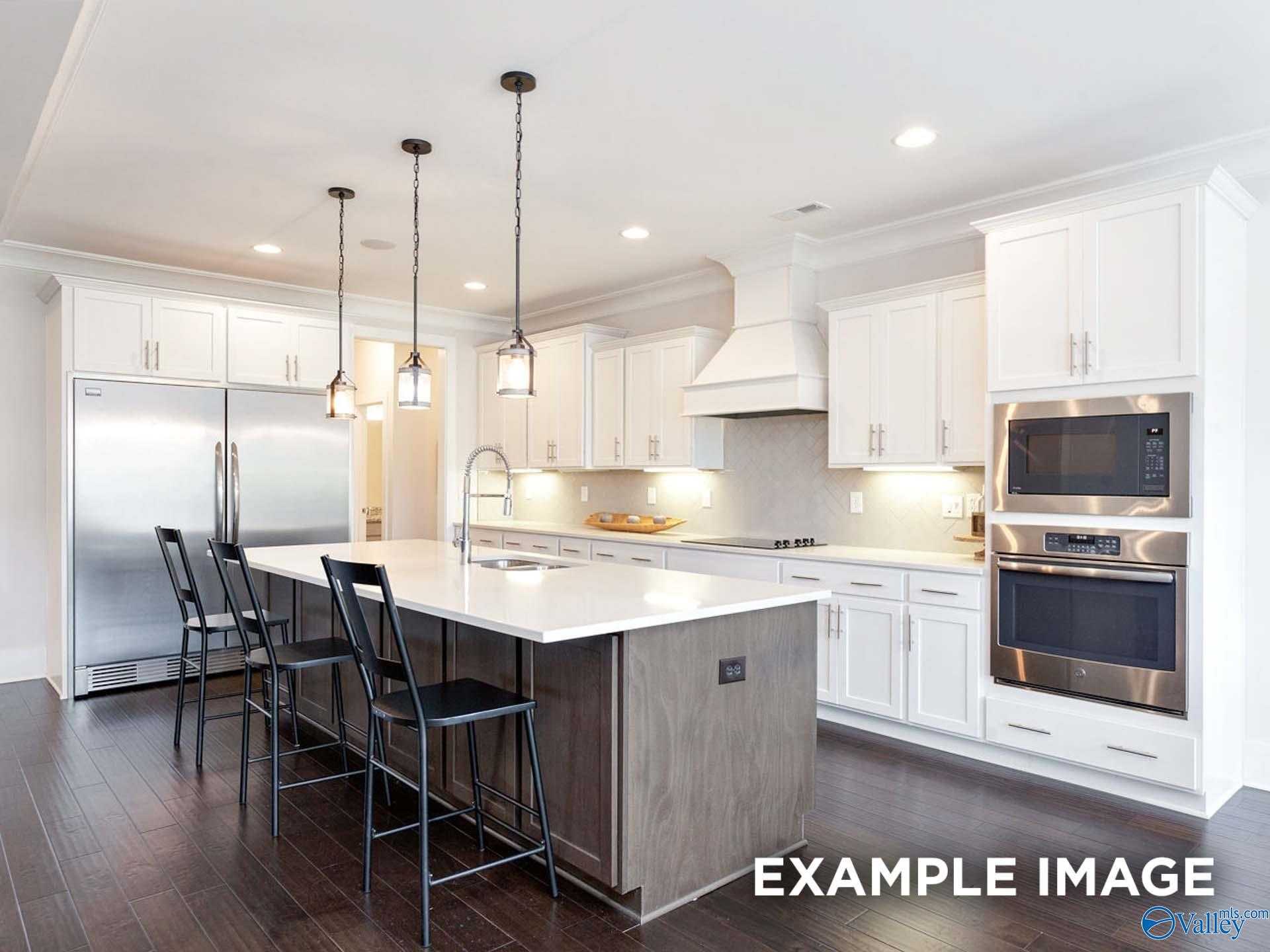 Modern white kitchen island with stainless appliances, pendant lights, and bar seating in Davidson Homes The Finleigh, Meridianville, Alabama