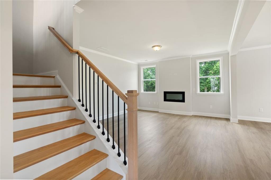Elegant oak staircase with black metal balusters in open foyer, modern gas fireplace, large windows, and hardwood floors in Davidson Homes The Willow B, Hoschton, GA