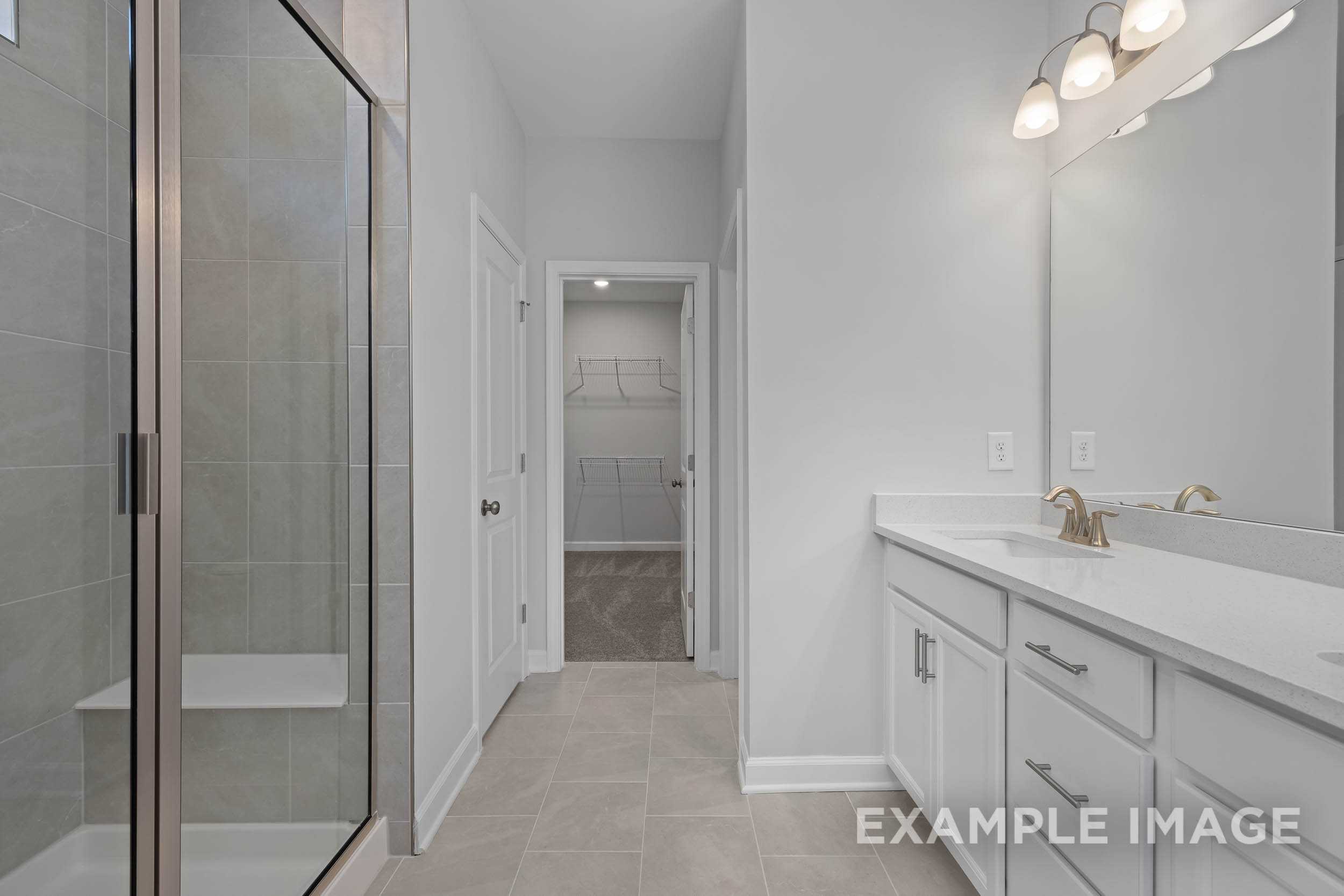 Spacious master bathroom in The Ash by Davidson Homes: frameless glass shower, double white vanity, large mirror, walk-in closet door