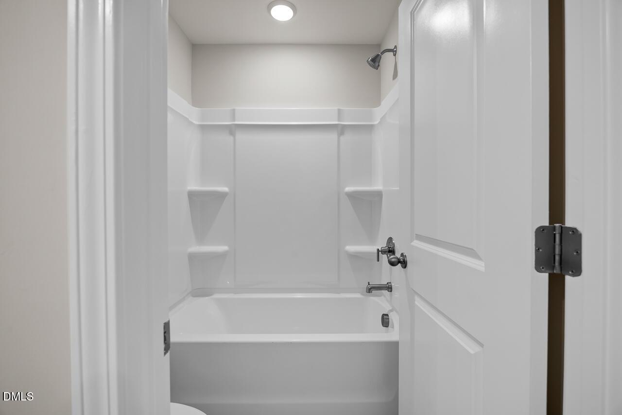 Modern white bathroom with tub-shower combo, built-in shelves, and fixtures in Davidson Homes The Avery, Knightdale, NC