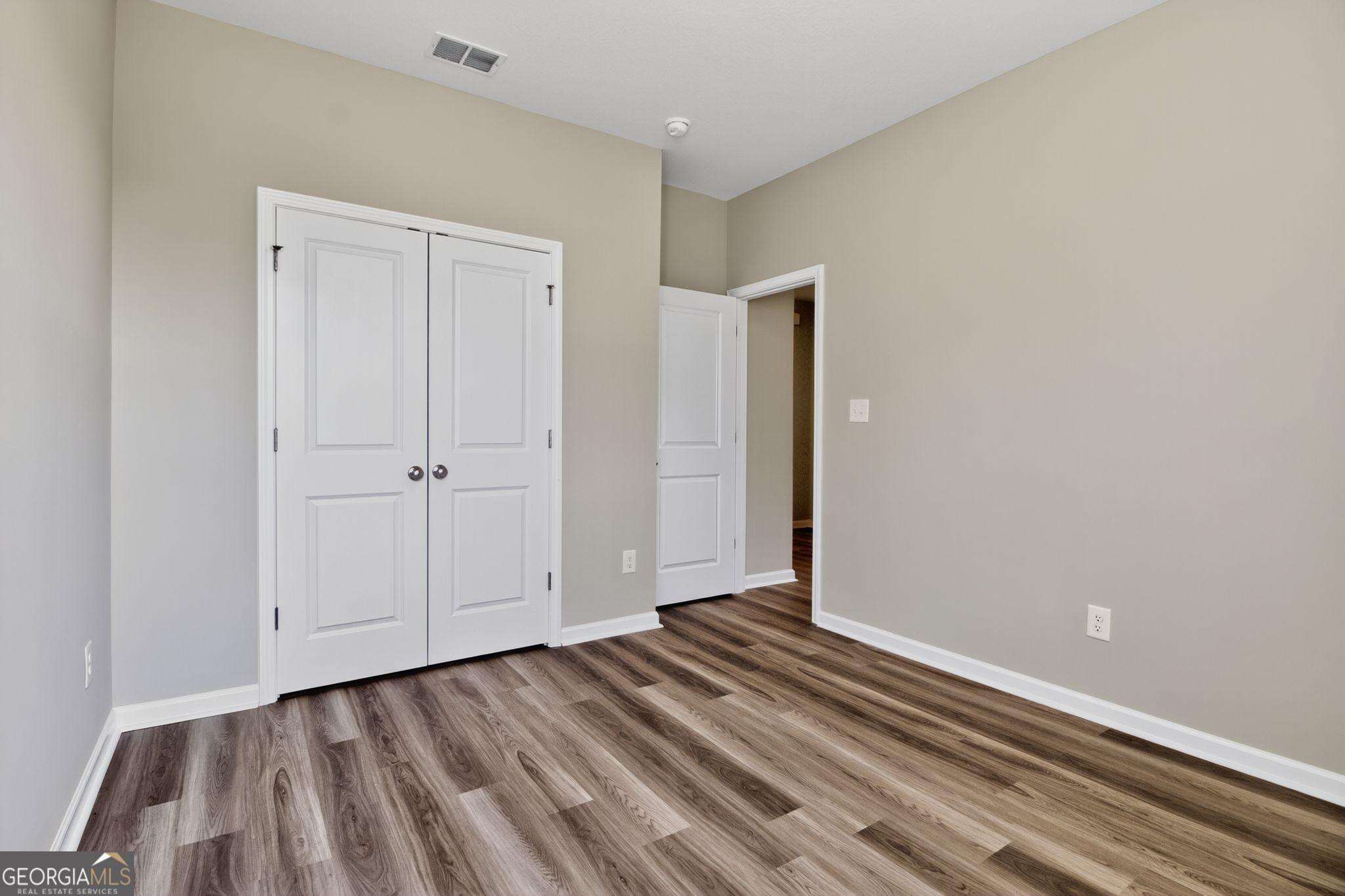 Spacious bedroom with walk-in closet, white doors, and luxury vinyl plank flooring in Evermore Homes The Luna, Ivy Glen, Perry, Georgia