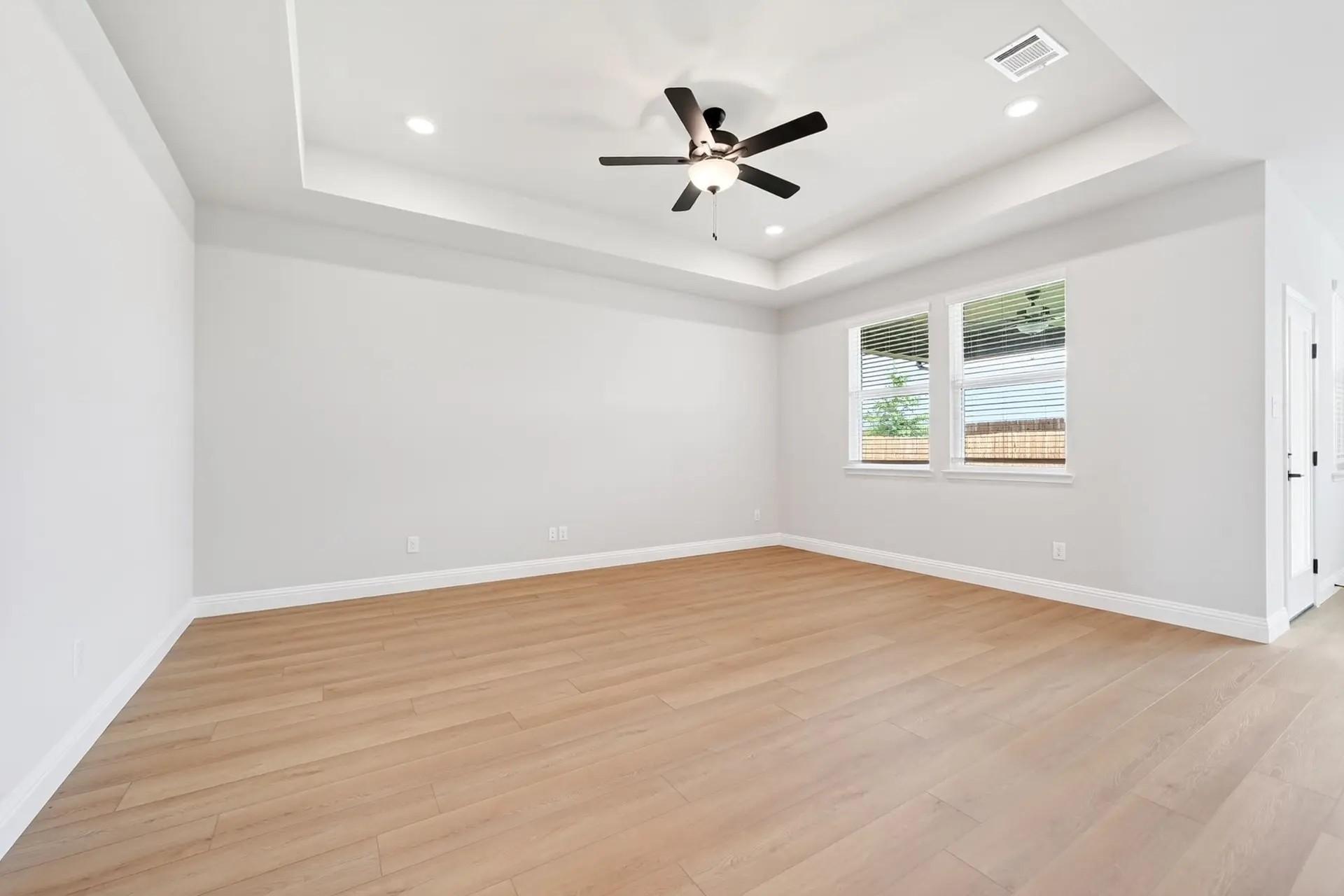 Spacious bedroom with tray ceiling and wood-look flooring in The Holly C floor plan by Davidson Homes in Heartland, Texas.
