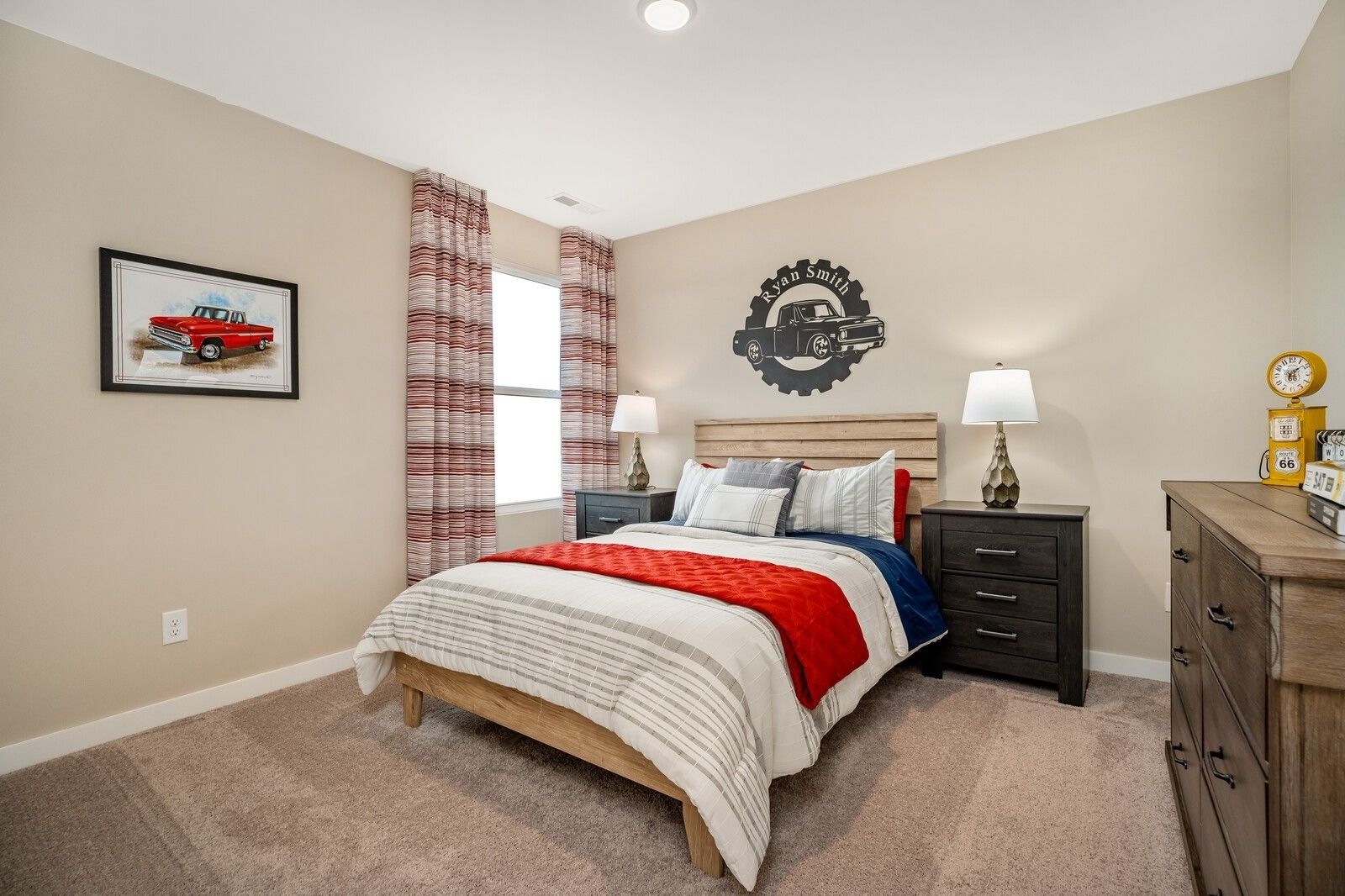 Boy's bedroom featuring truck-themed wall art, wooden bed with red throw, plaid curtains, and beige walls in Davidson Homes The Gordon C, White House, TN