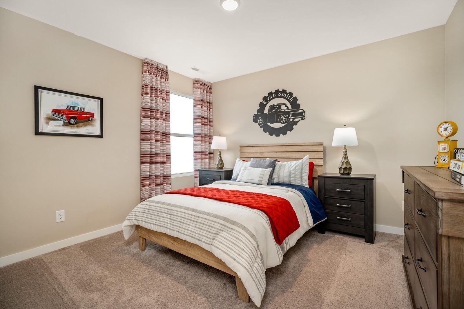Boy's bedroom featuring truck-themed wall art, wooden bed with red throw, plaid curtains, and beige walls in Davidson Homes The Gordon C, White House, TN