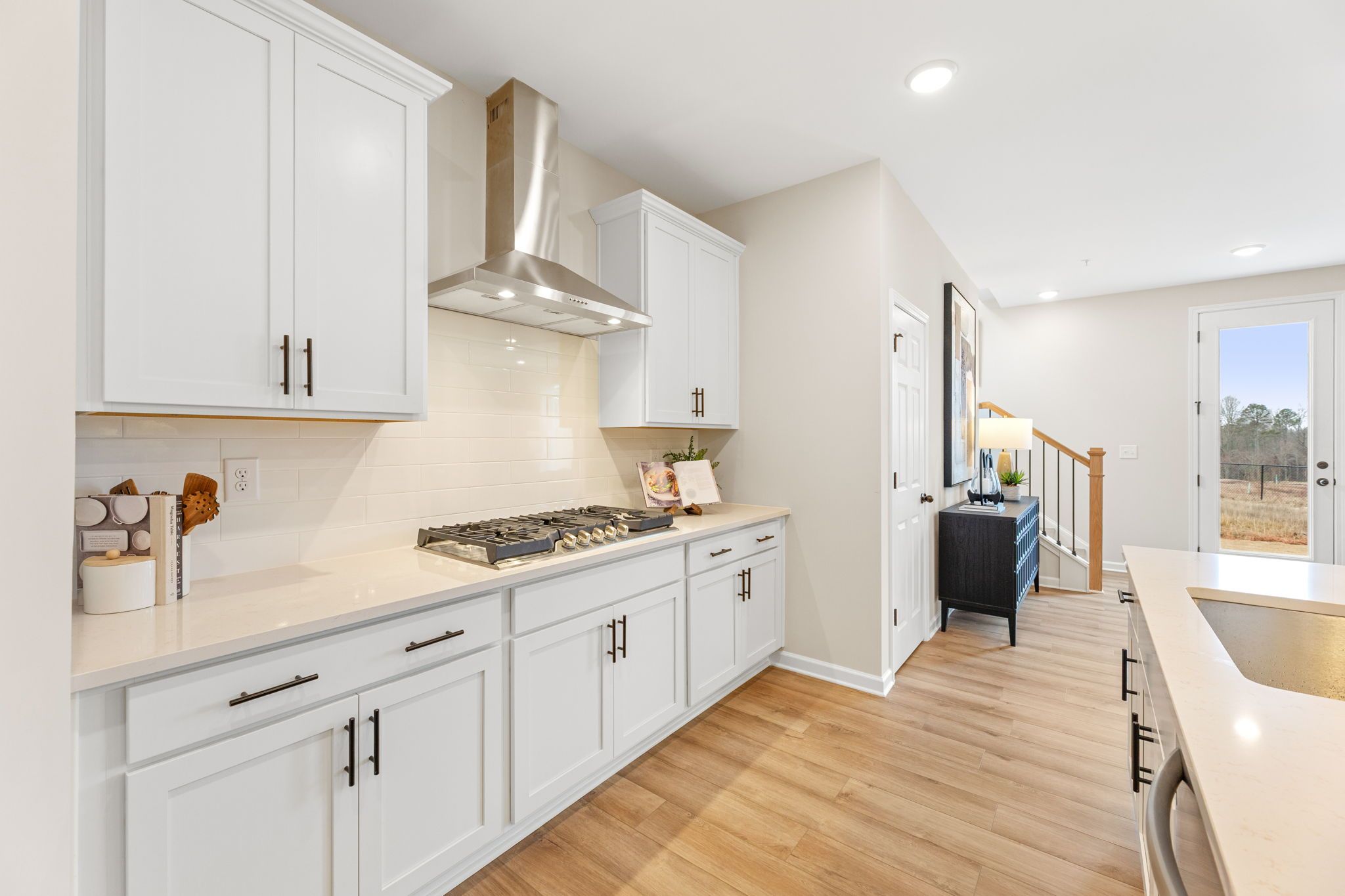 Spacious white kitchen in Hemingway Cumming GA with shaker cabinets, quartz island, stainless steel range, and hardwood floors by Davidson Homes