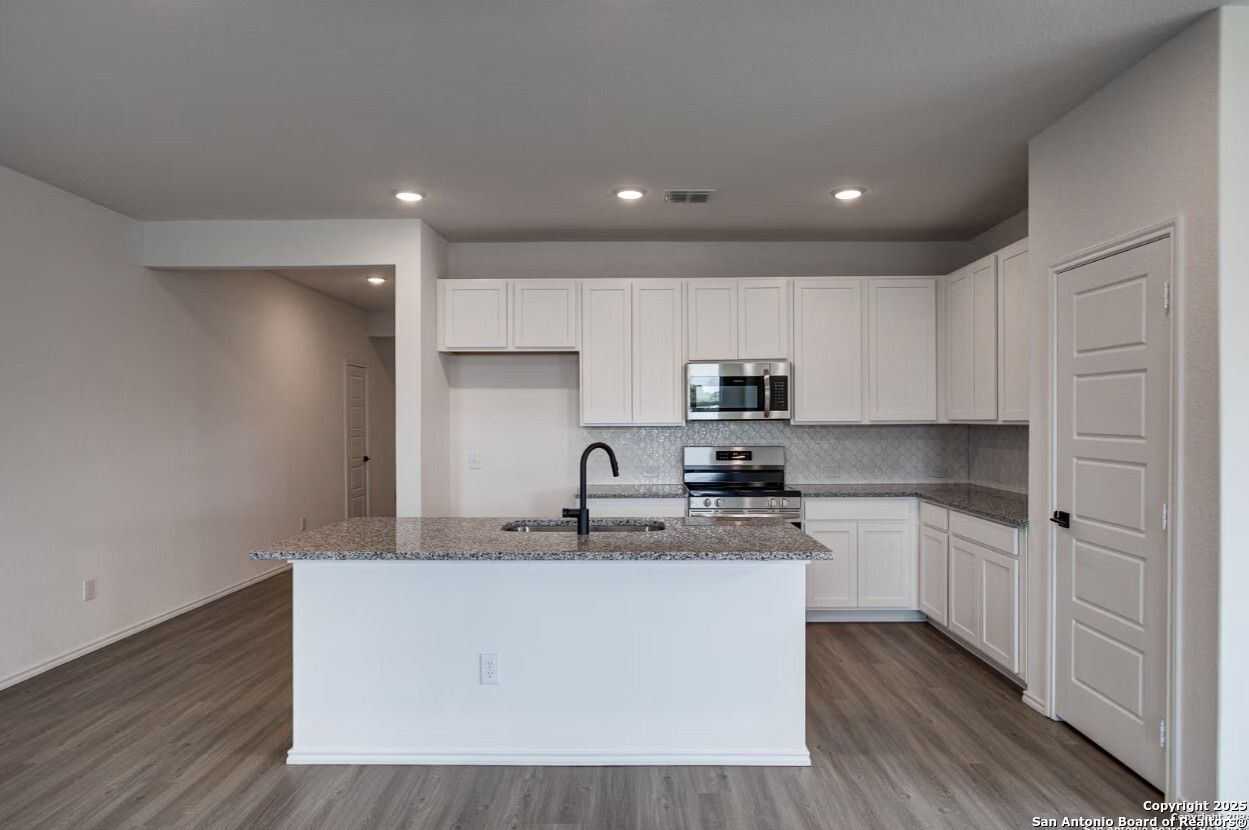 Modern open-concept kitchen with white shaker cabinets, granite countertops, stainless appliances, and large island in The Daphne H, Seguin, Texas