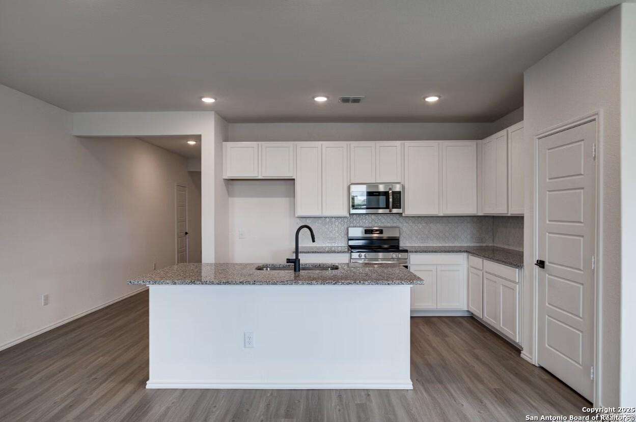 Modern open-concept kitchen with white shaker cabinets, granite countertops, stainless appliances, and large island in The Daphne H, Seguin, Texas