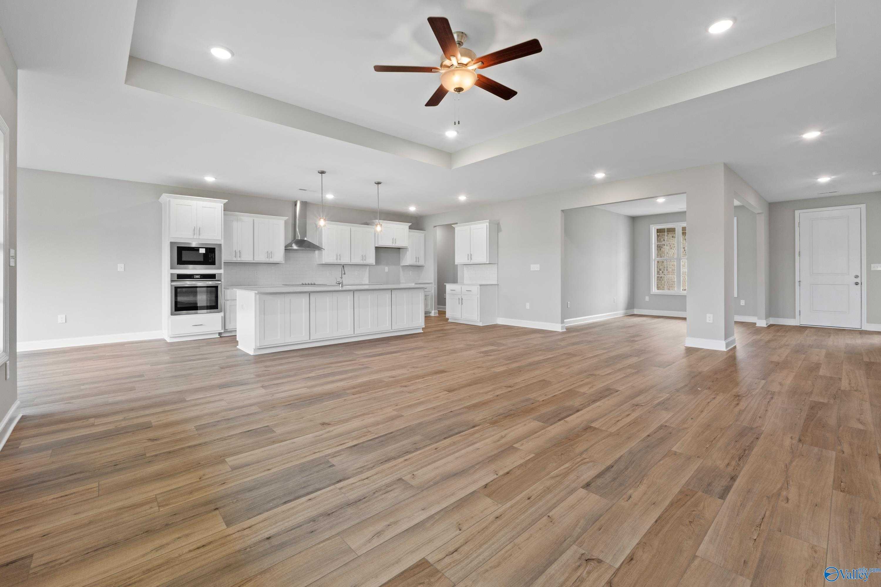 Modern open-concept kitchen with white shaker cabinets, stainless double ovens, island, hardwood floors, and ceiling fan in The Finleigh, Meridianville, AL