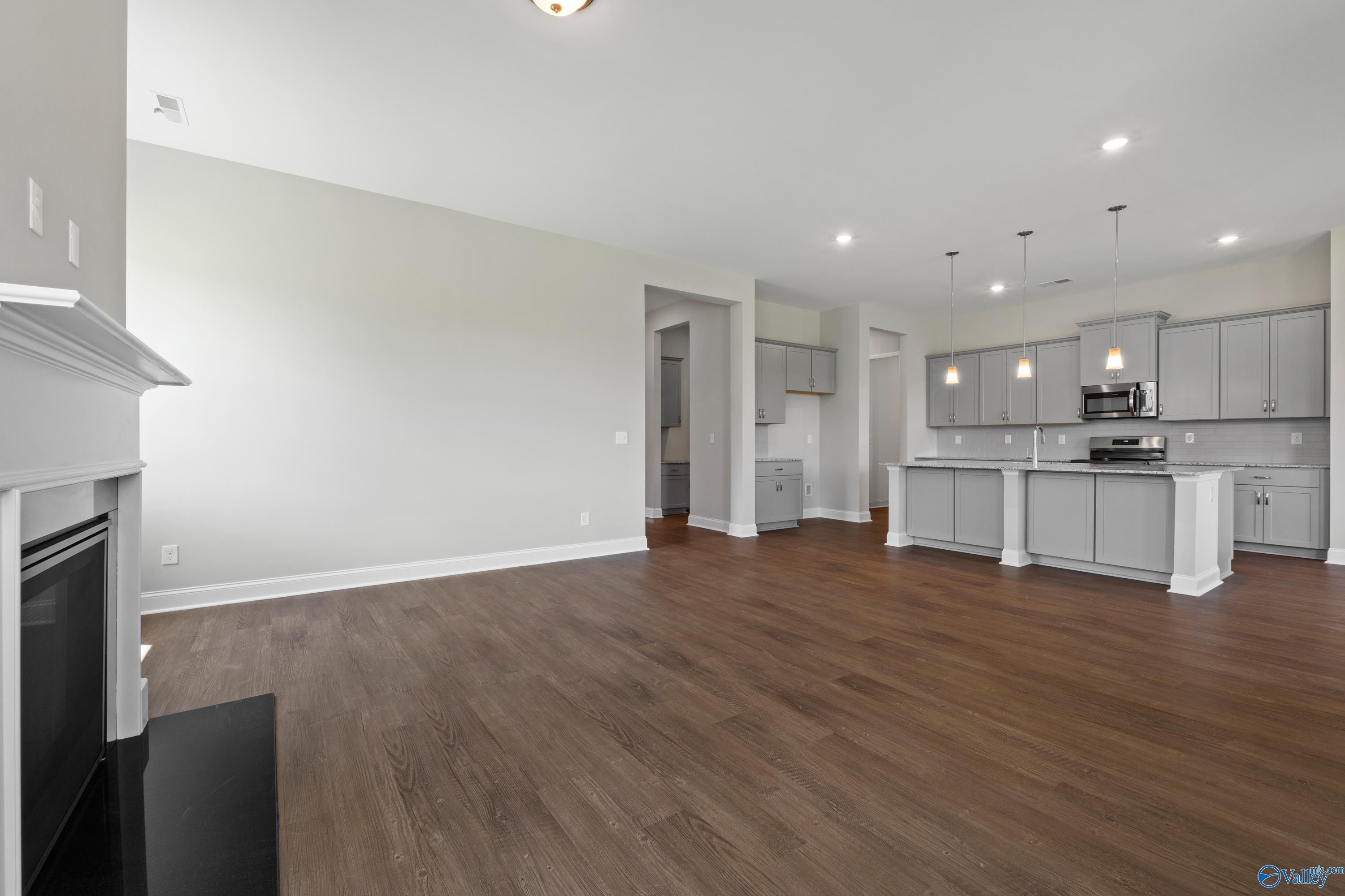 Open-concept living room with white mantel gas fireplace and adjacent kitchen with gray cabinets, island, hardwood floors in The Arcadia B, Huntsville