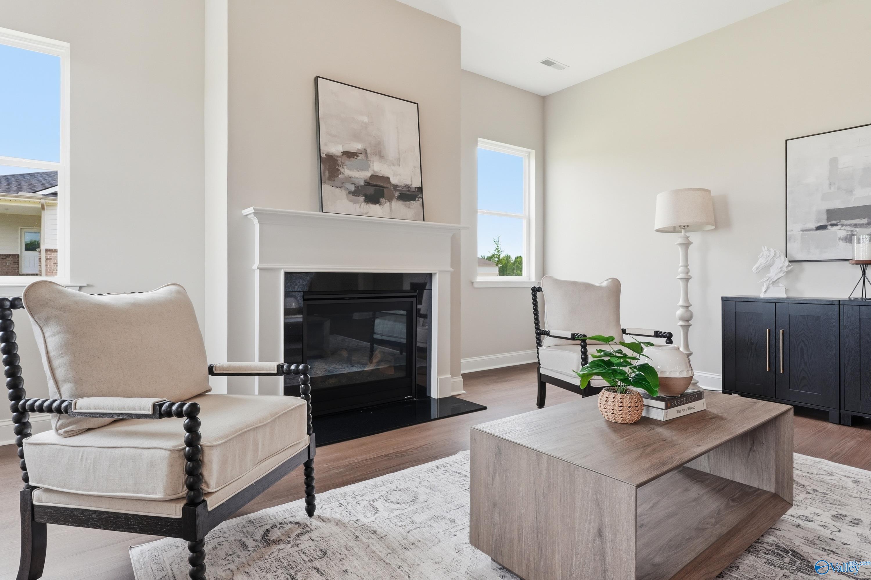 Cozy living room featuring white mantel fireplace, beige armchairs, and hardwood floors in Davidson Homes Arcadia B, Huntsville AL