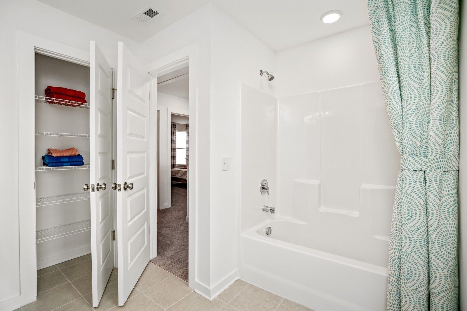 Bright bathroom with open linen closet, folded towels, white tub-shower combo, teal patterned curtain in Davidson Homes The Gordon C, White House, TN