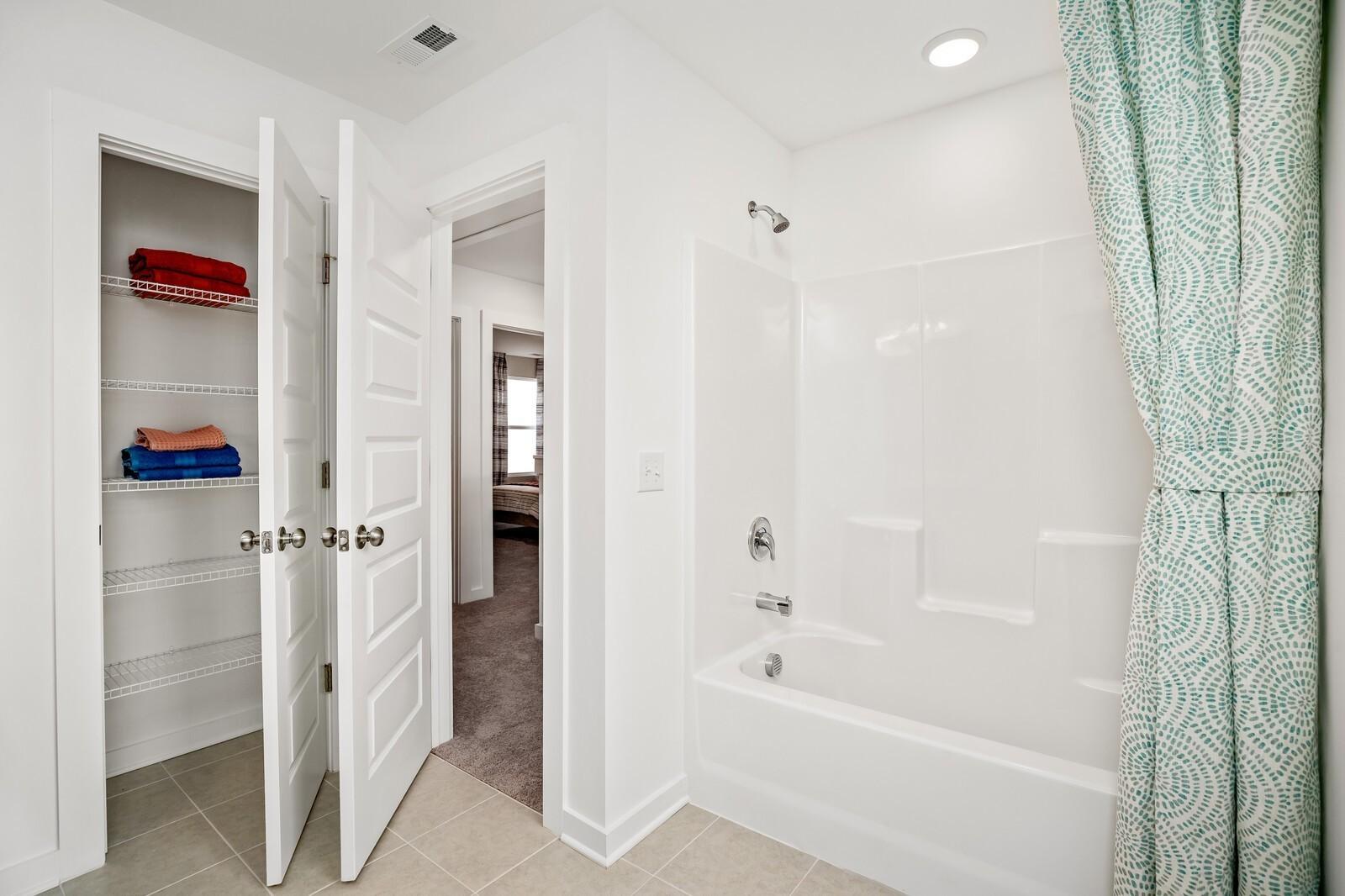 Bright bathroom with open linen closet, folded towels, white tub-shower combo, teal patterned curtain in Davidson Homes The Gordon C, White House, TN