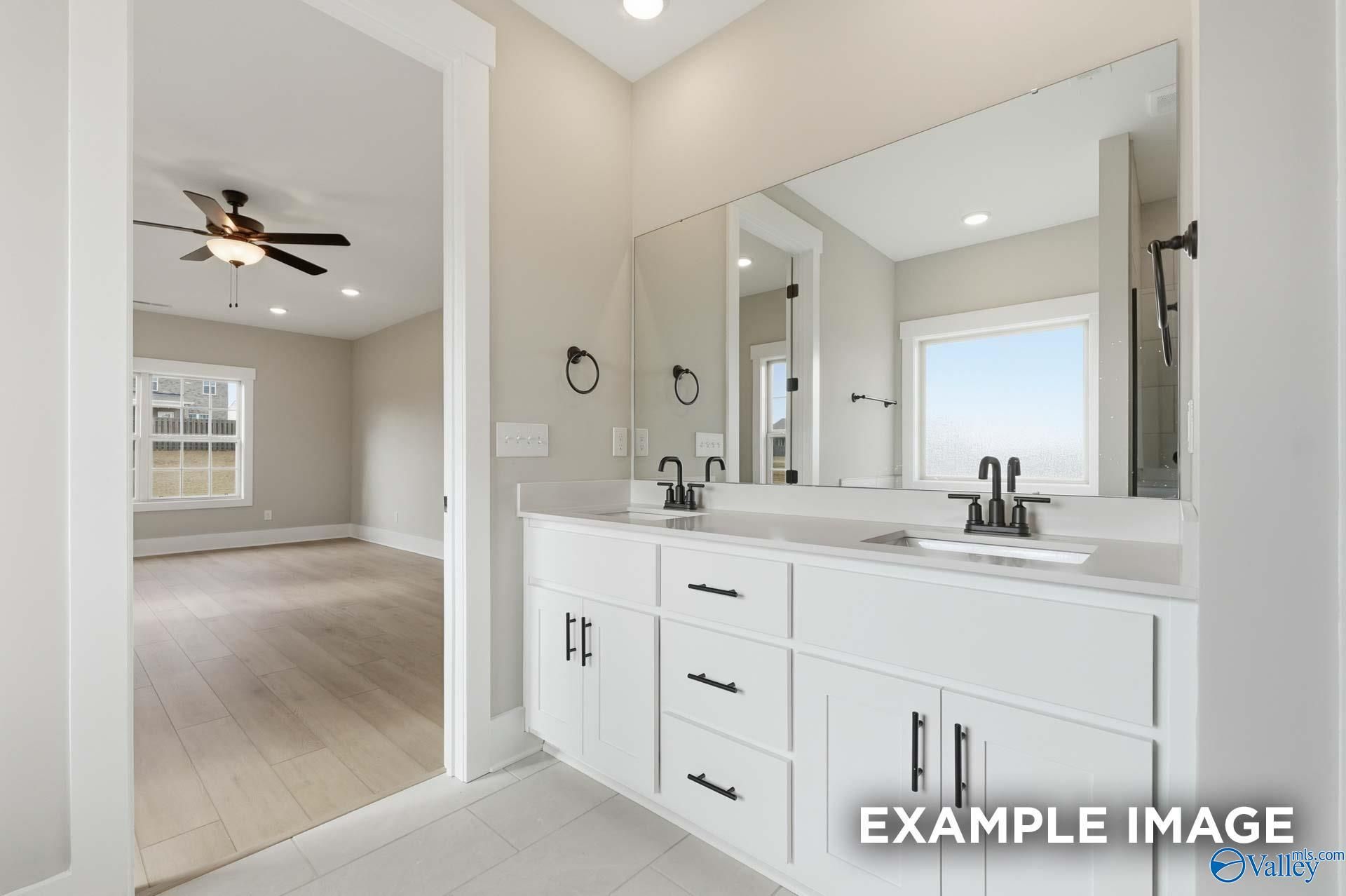 Modern master bathroom double vanity with white cabinets, mirrors, and adjacent bedroom in Davidson Homes The Emory, Decatur, Alabama