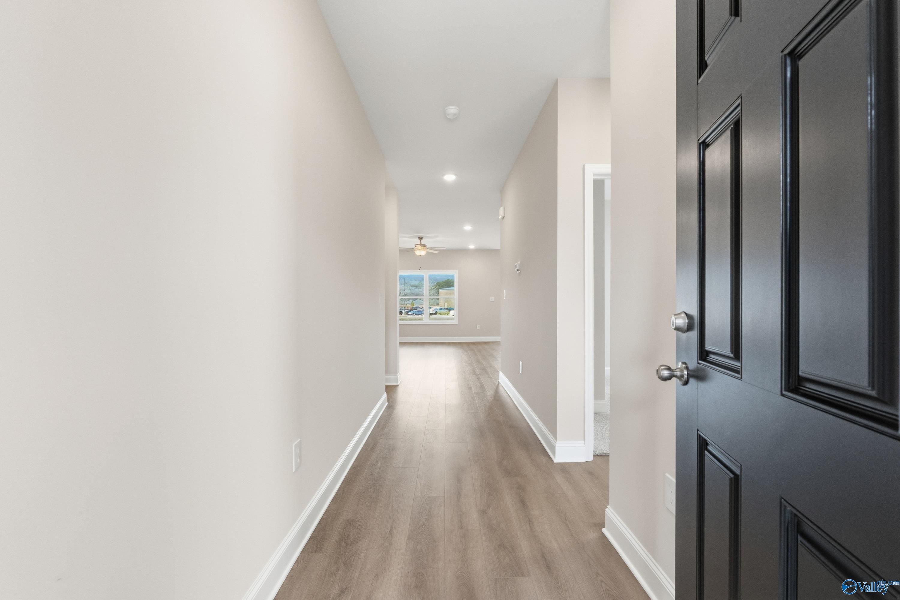 Bright hallway with light walls, wood-look flooring, open black door, and window view in The Asheville C home, Huntsville, AL