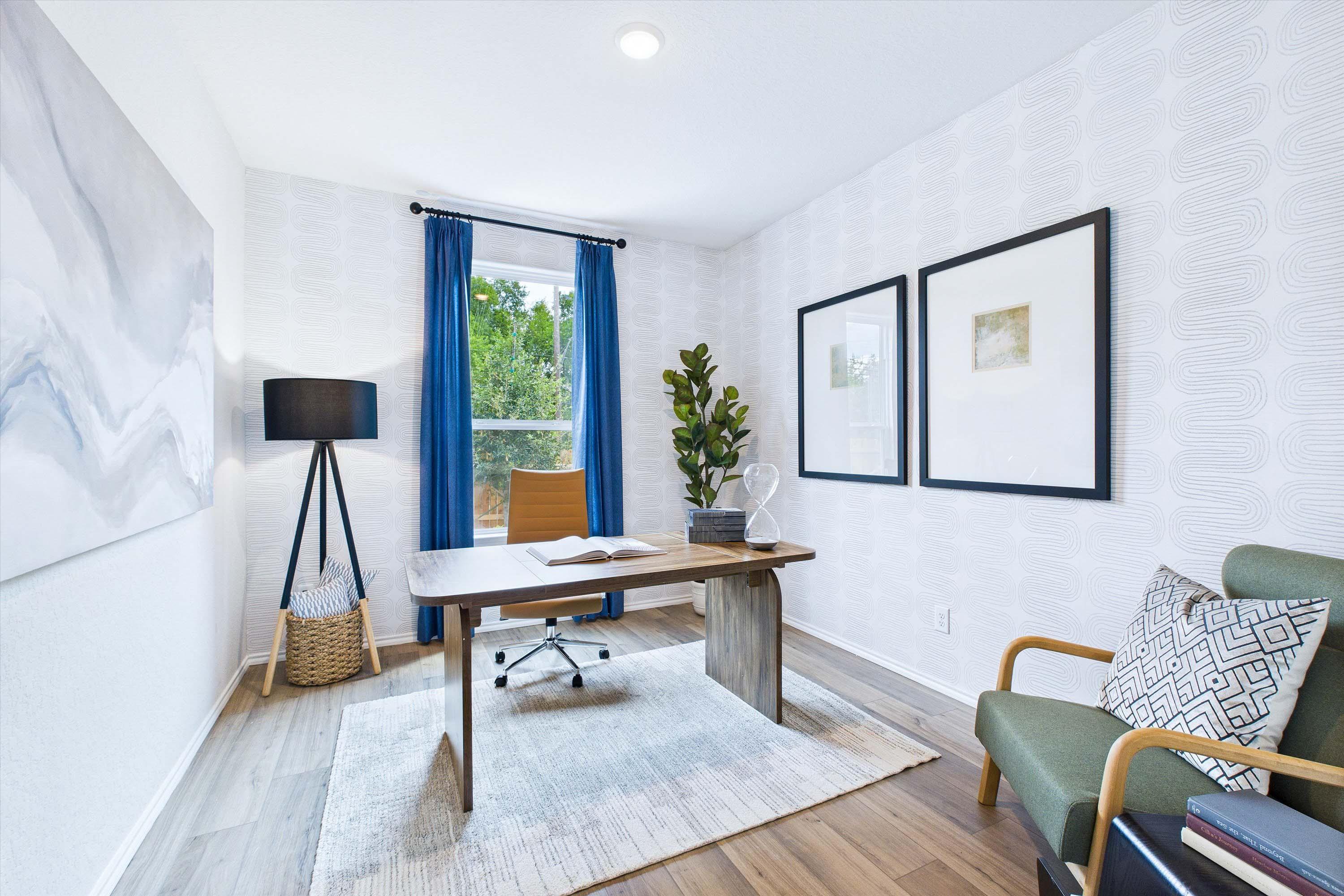 Modern home office in The Gillian C floor plan featuring a wood desk, patterned wallpaper, and blue curtains in San Antonio.
