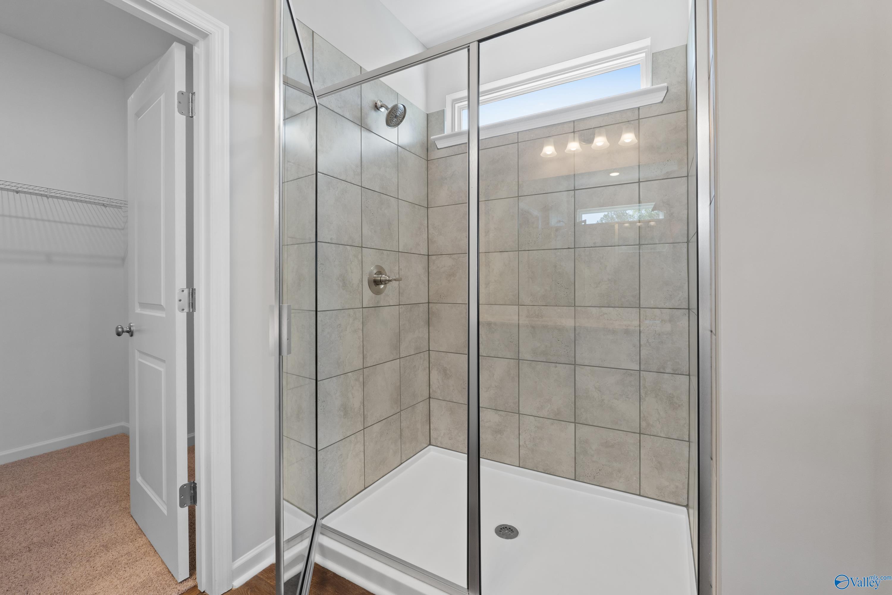 Modern frameless glass shower with subway tile walls and transom window in Evermore Homes The Noble, Madison Alabama