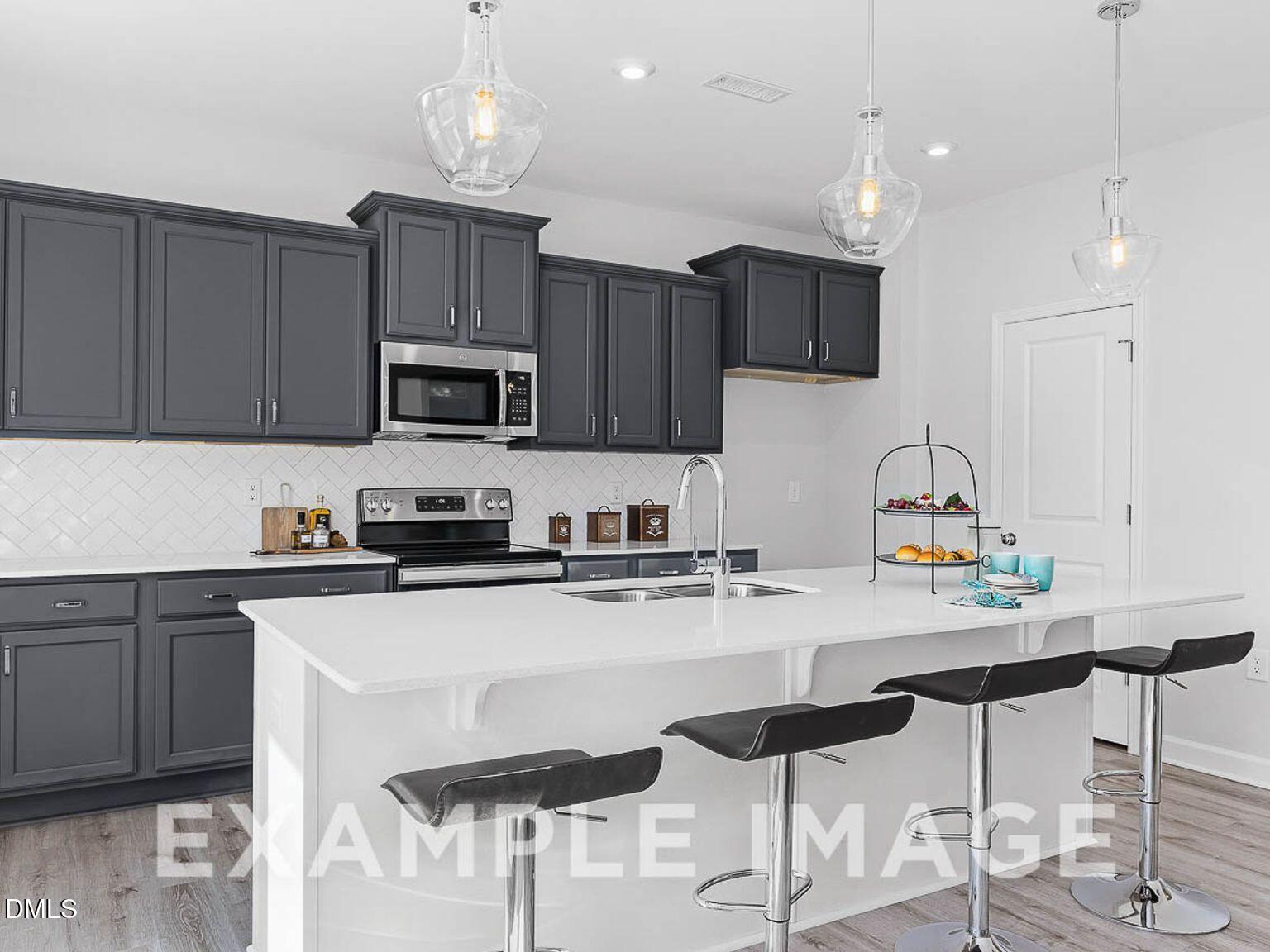 Modern kitchen with gray shaker cabinets, white quartz island, bar seating, stainless appliances in The Chestnut B, Lillington, NC
