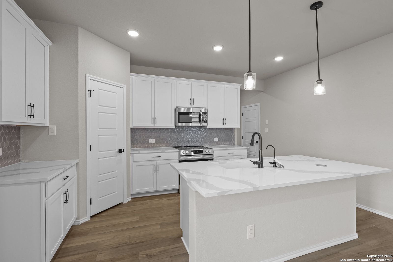 Modern white kitchen with quartz island sink, stainless appliances, pendant lights in Davidson Homes The Murray J, San Antonio