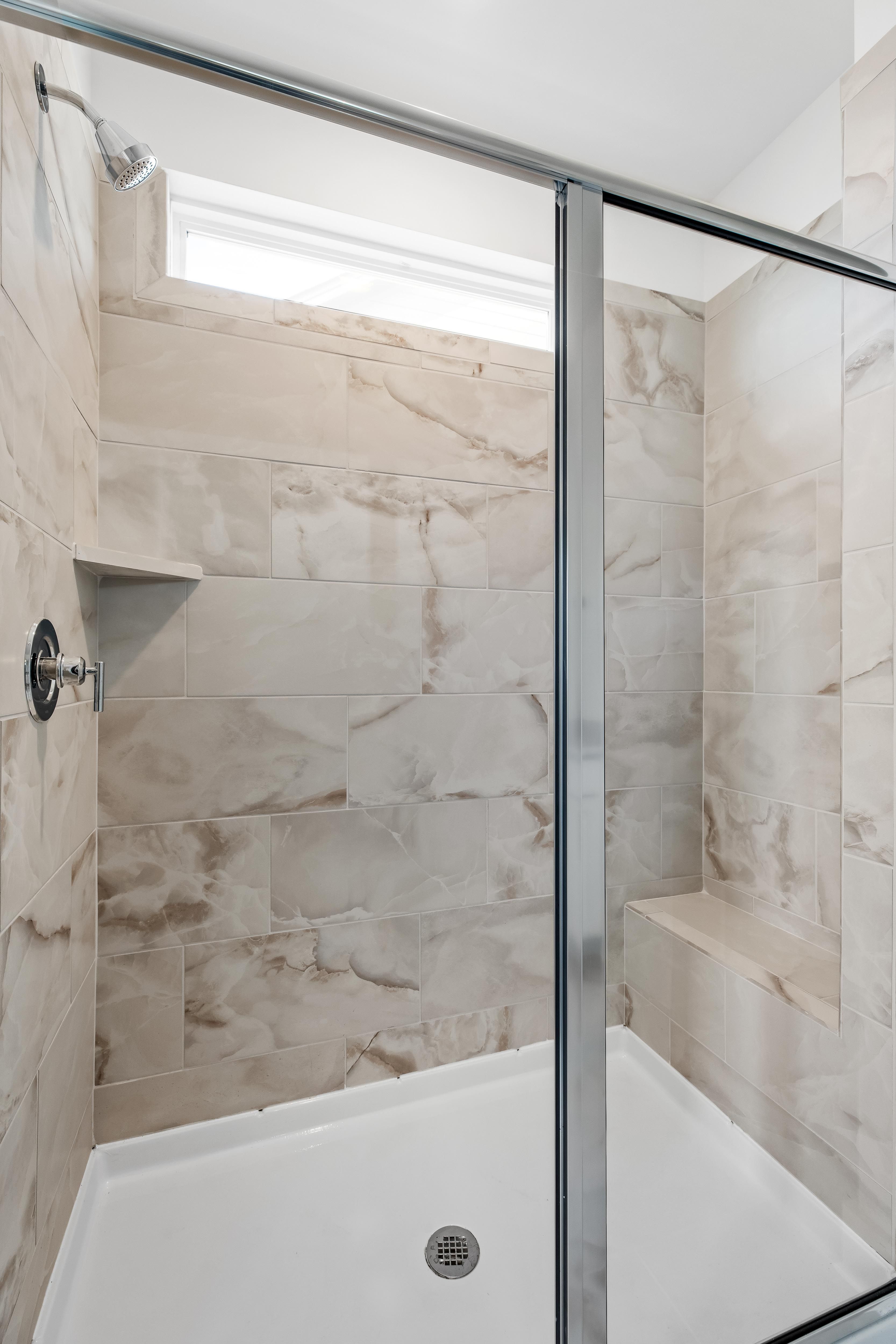 Modern walk-in shower with marble-look tile and built-in bench in The Cedar D master bathroom by Davidson Homes.