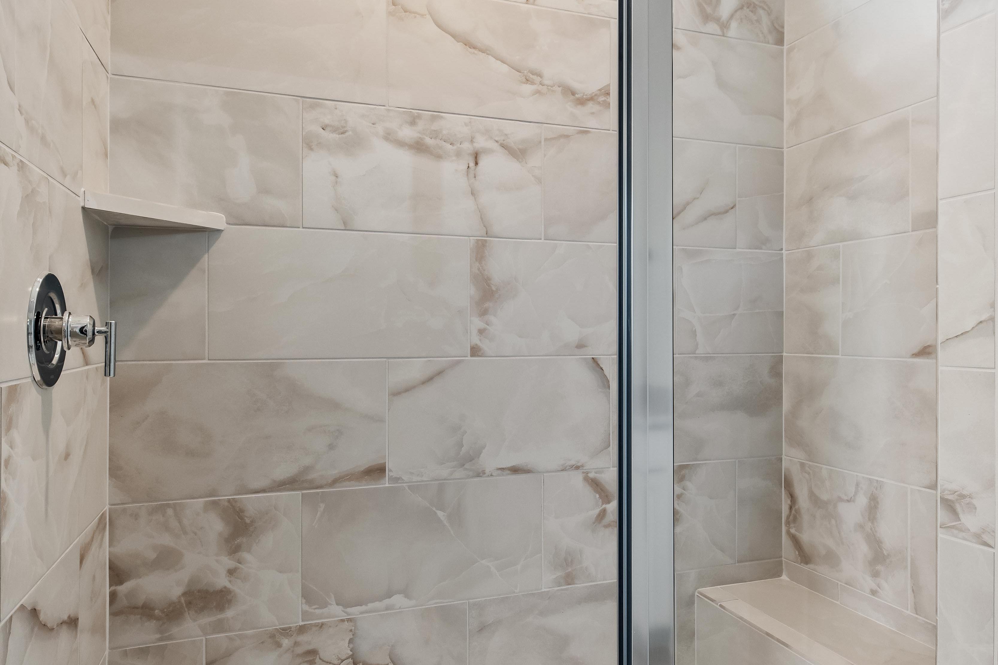 Modern walk-in shower with marble-look tile and built-in bench in The Cedar D master bathroom by Davidson Homes.