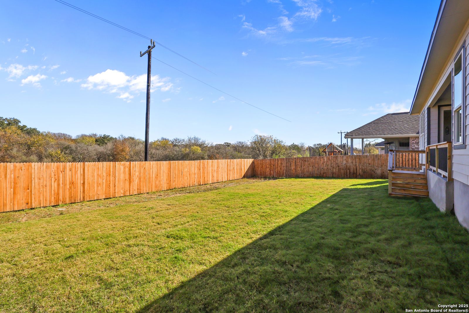 Private fenced backyard with lush green lawn, wooden privacy fence, and covered deck in 5-bedroom Davidson Homes Jennings G, Castroville, TX