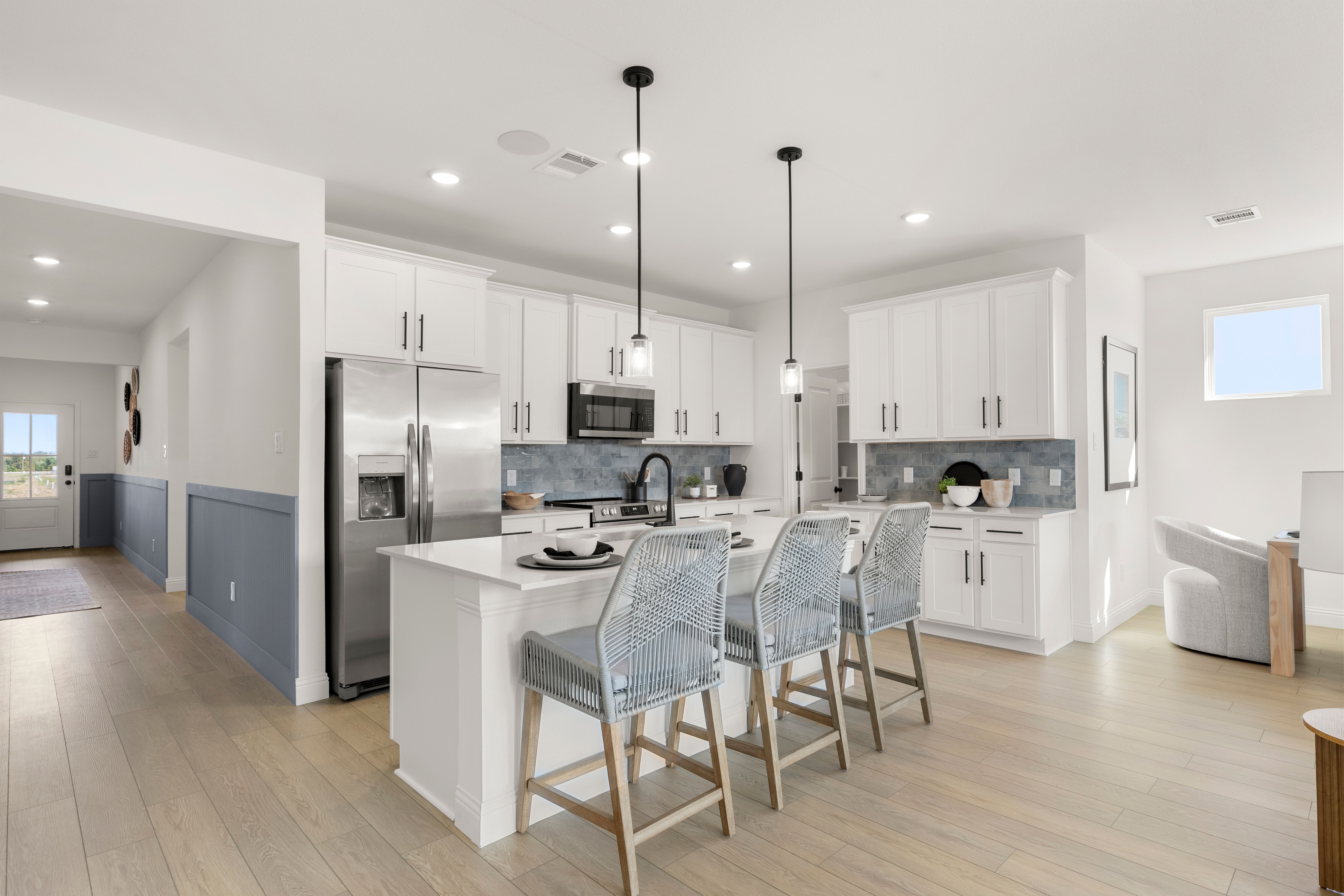 Modern kitchen in The Laurel I by Davidson Homes featuring white shaker cabinets, large quartz island, stainless steel appliances, blue rattan stools