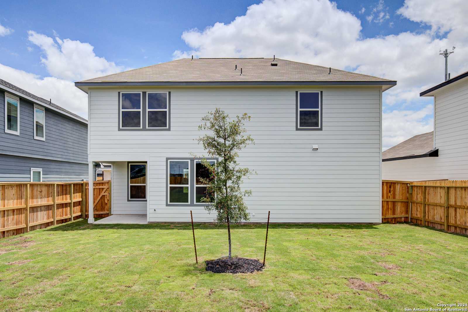 Covered back patio and spacious grassy backyard with young tree and wooden fence in Davidson Homes The Murray H, Seguin, Texas