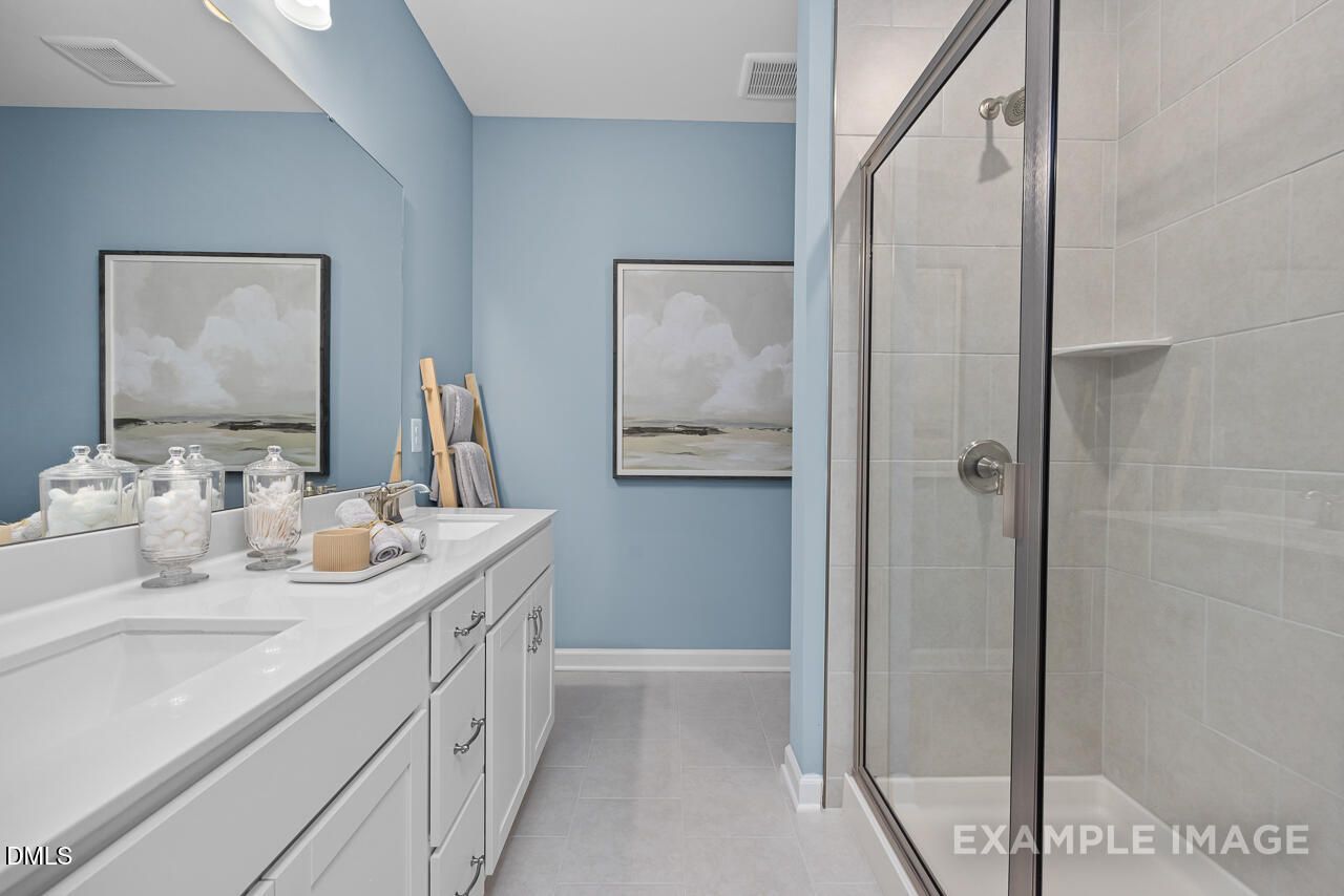 Elegant master bathroom with light blue walls, white double vanity, and glass shower in Davidson Homes Magnolia D, Angier, NC