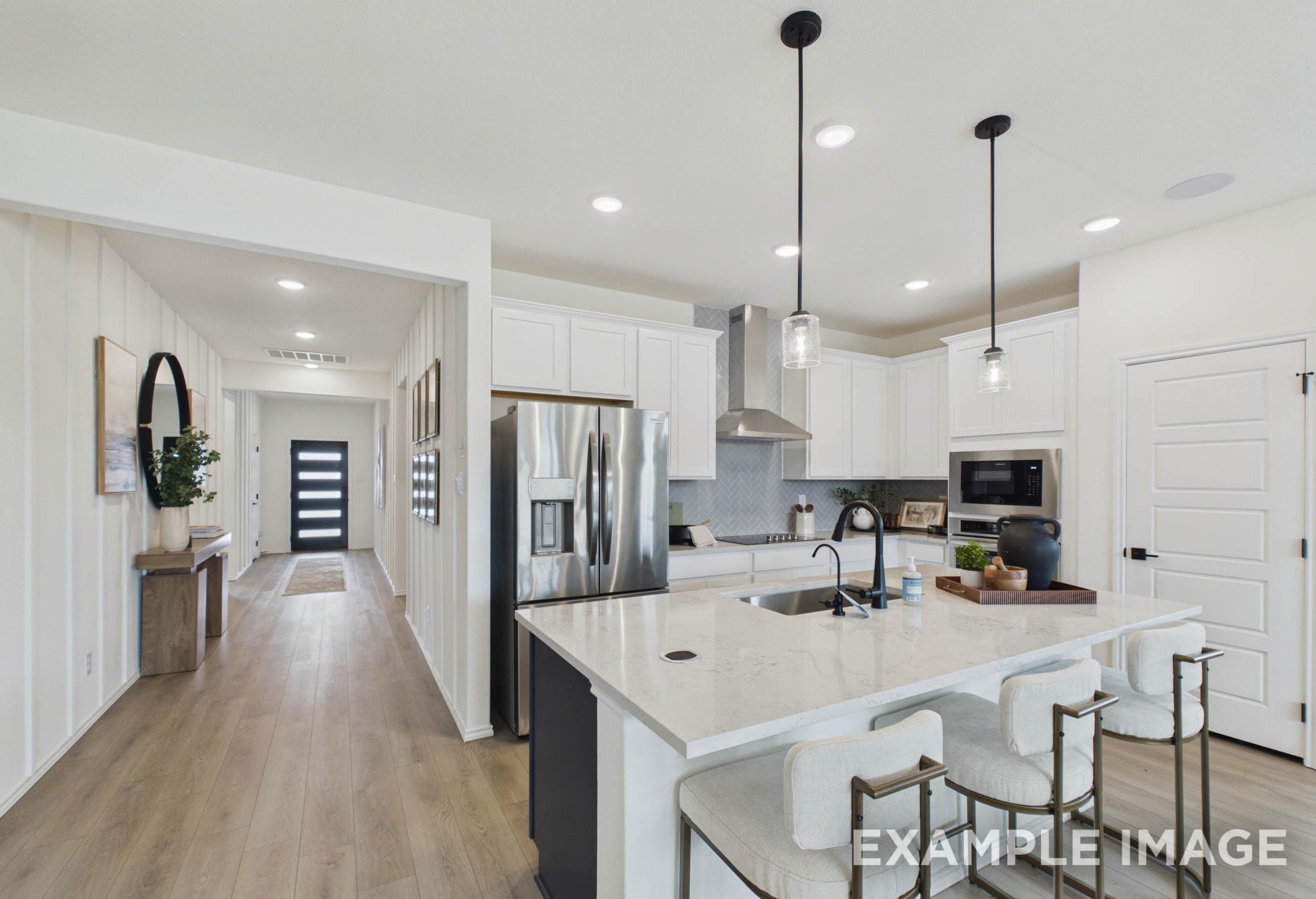 Modern open-concept kitchen in The Laurel G featuring a large quartz island, stainless steel appliances, and white cabinetry.