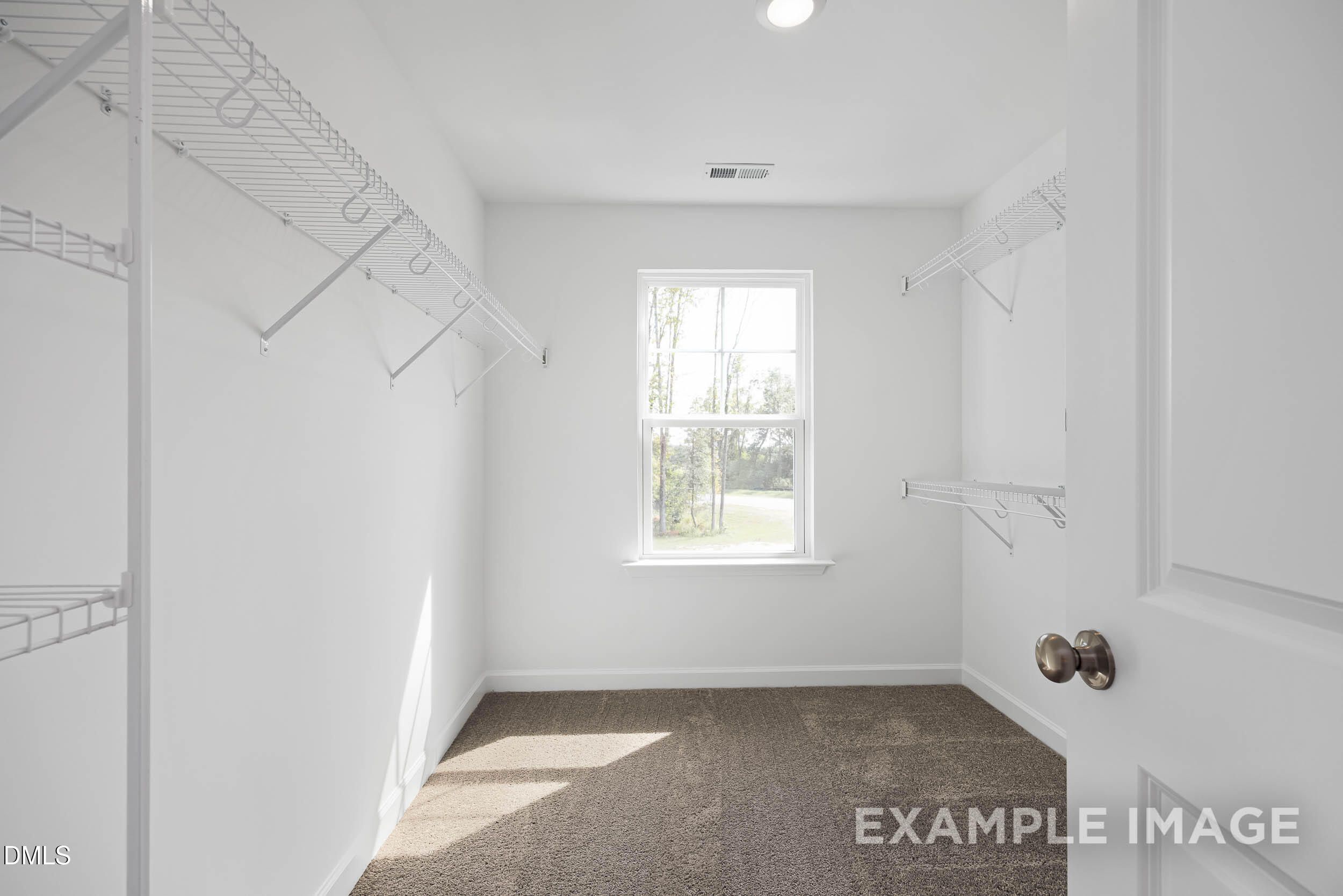 Spacious walk-in closet with wire shelving, hanging rods, and sunlit window in Davidson Homes The Willow D, Zebulon, NC