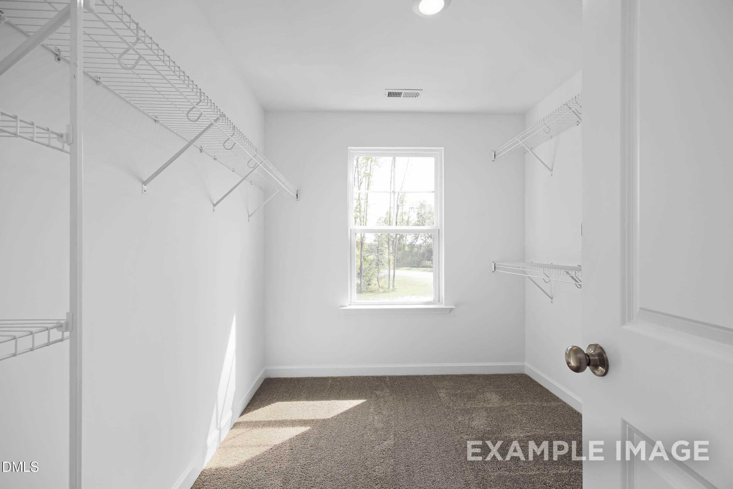 Spacious walk-in closet with wire shelving, hanging rods, and sunlit window in Davidson Homes The Willow D, Zebulon, NC