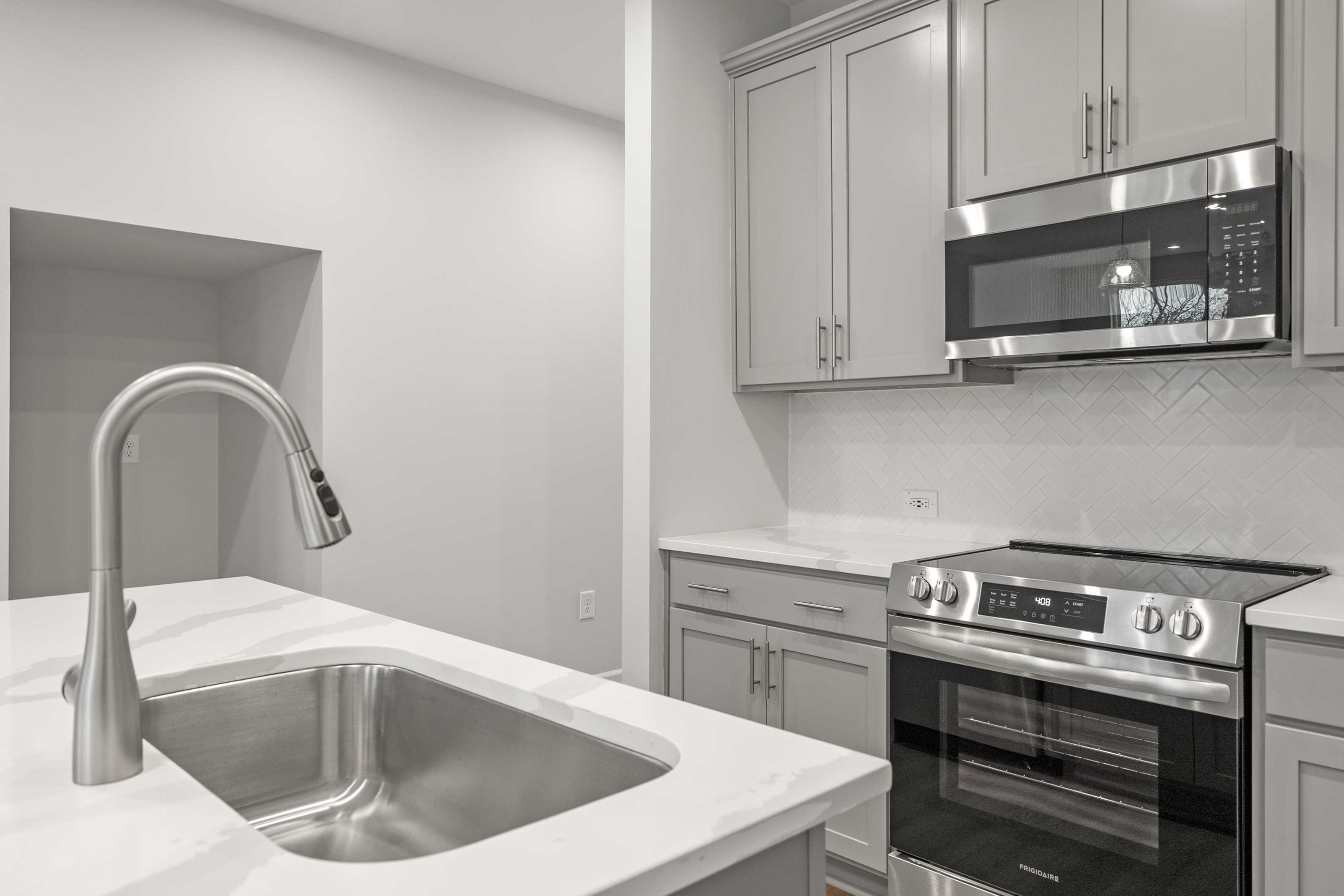 Modern kitchen in The Durant A by Davidson Homes with white shaker cabinets, stainless steel appliances, island sink, and subway tile backsplash
