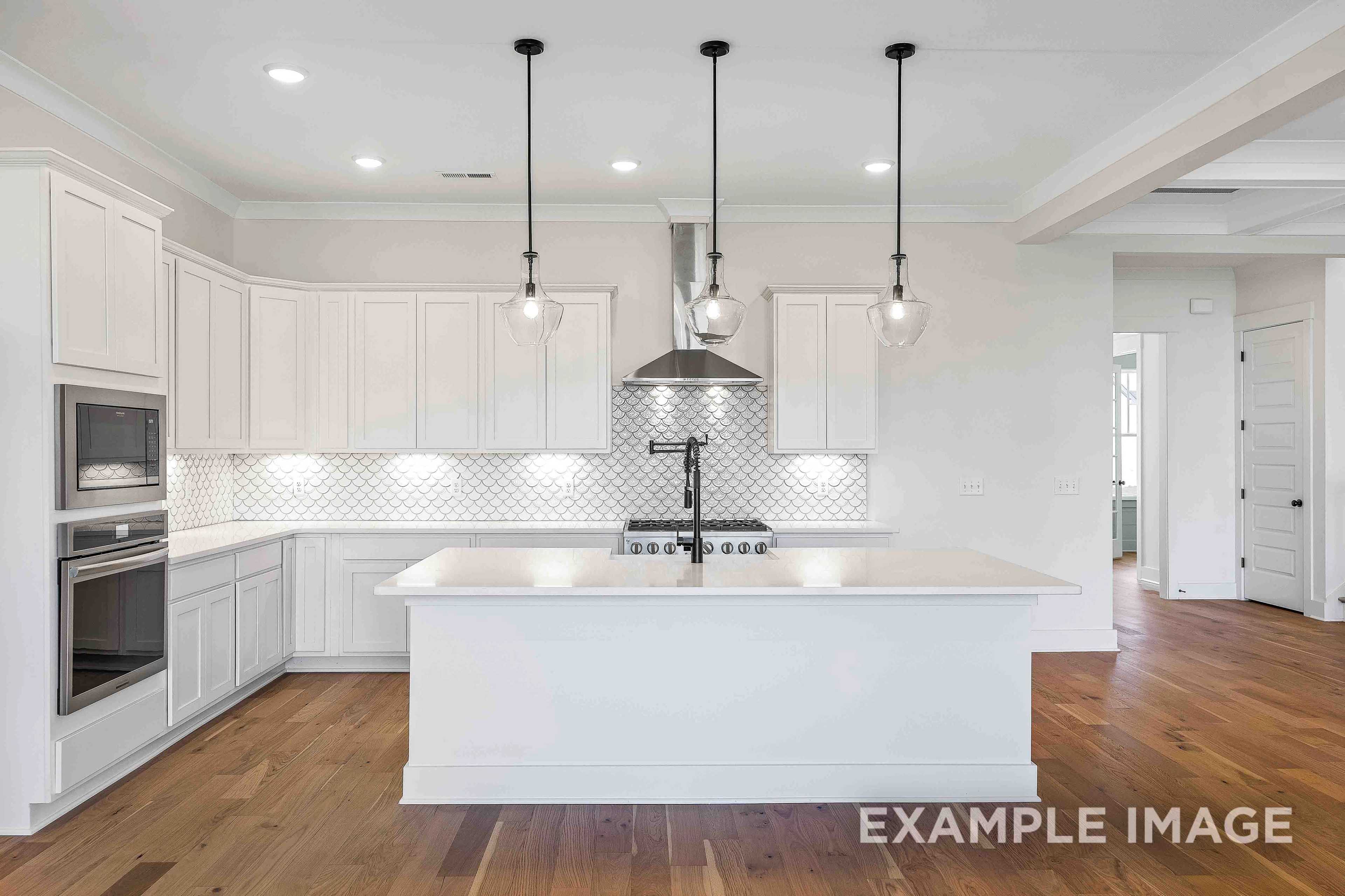 Spacious white kitchen in The Albany A with shaker cabinets, large island, stainless steel appliances, subway tile backsplash, and pendant lights