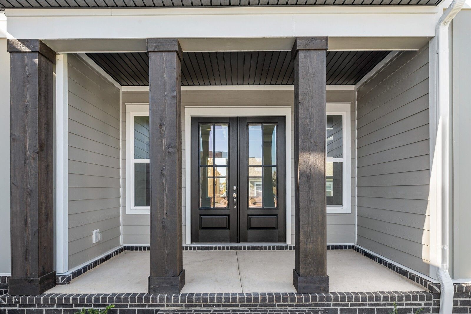Elegant front porch with dark wooden columns, double black doors, and gray siding on The Alston A home in Shelton Square, Murfreesboro, TN