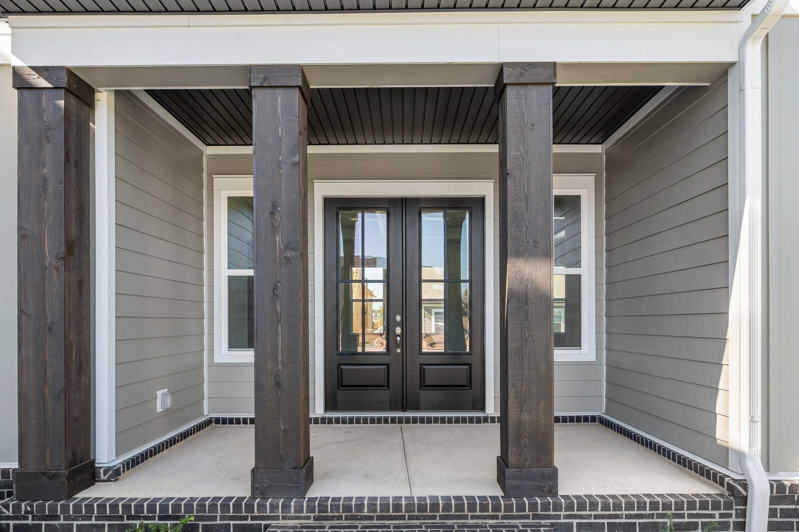 Elegant front porch with dark wooden columns, double black doors, and gray siding on The Alston A home in Shelton Square, Murfreesboro, TN