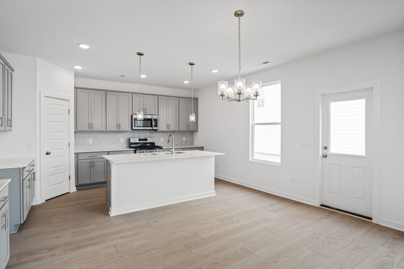 Modern kitchen with gray cabinets, white island, and hardwood floors in The Logan B floor plan at Calista Farms, TN.