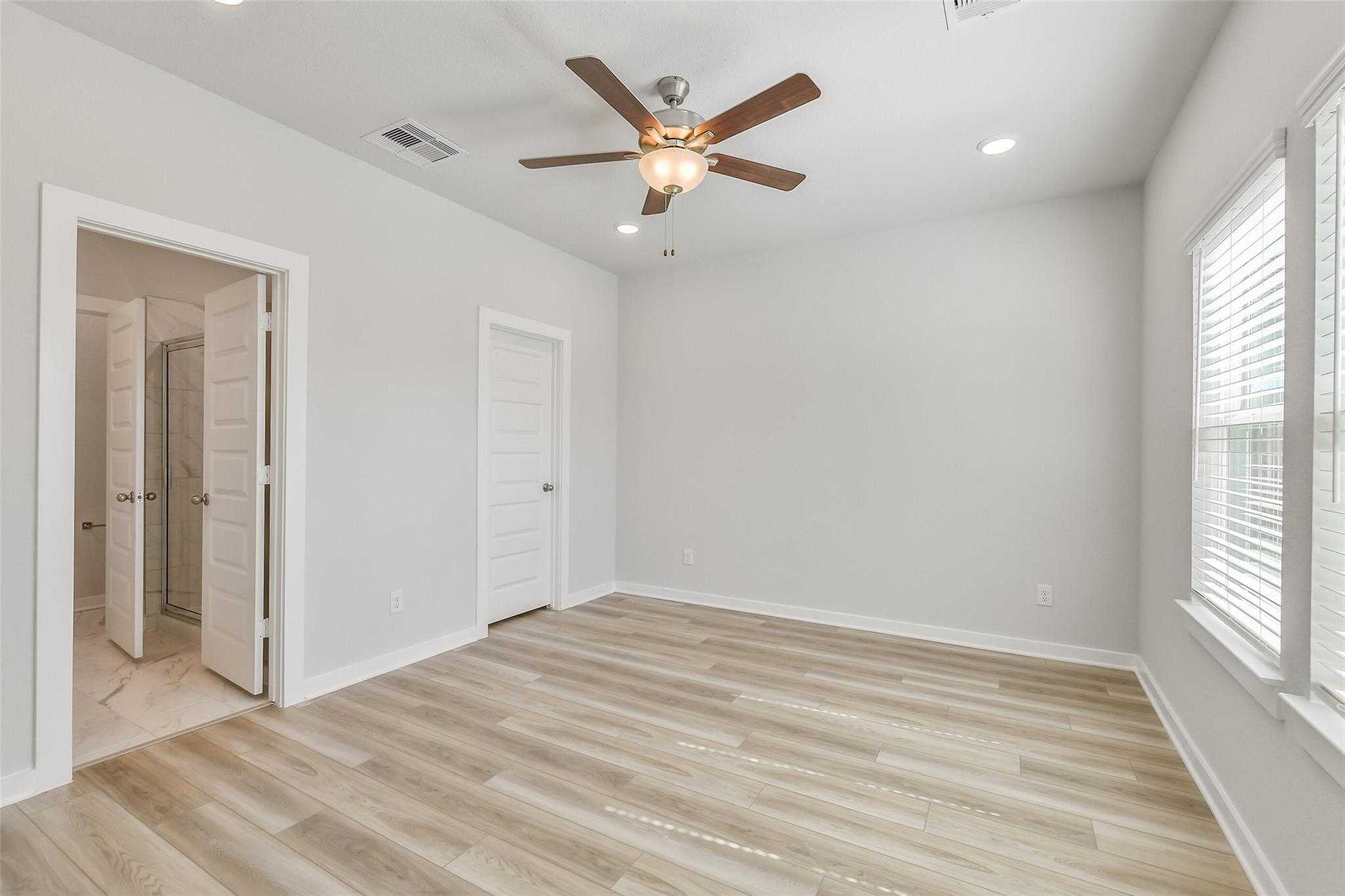 Spacious empty bedroom with ceiling fan, large blinds-covered windows, and adjacent bath in Davidson Homes The Rio Grande H, Magnolia TX