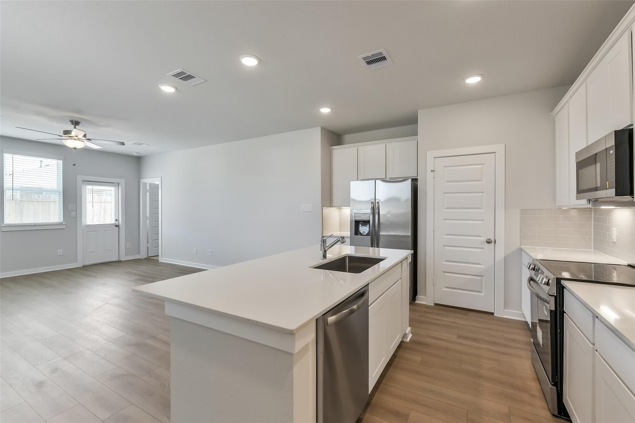 Modern open kitchen with white cabinets, quartz island, stainless steel appliances in Davidson Homes The Colorado F, Cleveland, Texas