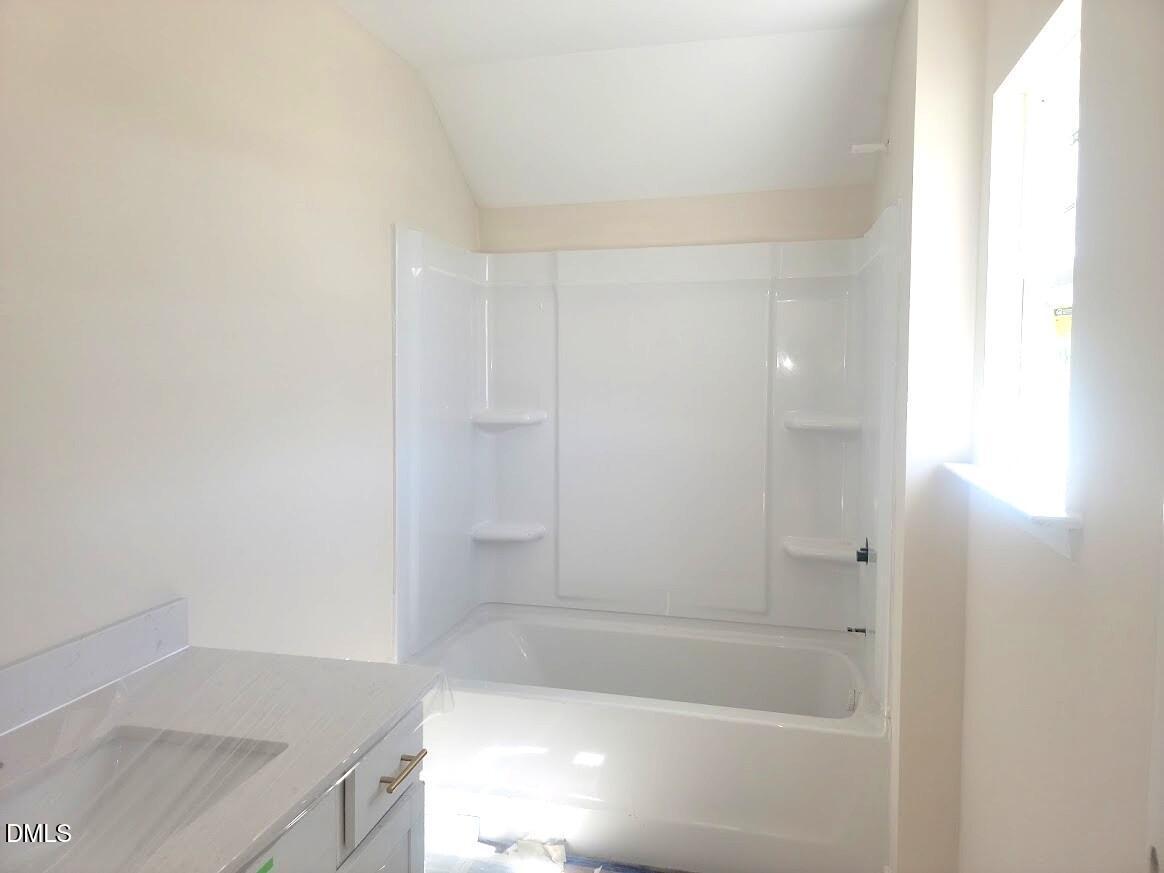 Bright guest bathroom with white tub, shower combo, and vanity in Davidson Homes The Cypress B II, Angier, NC