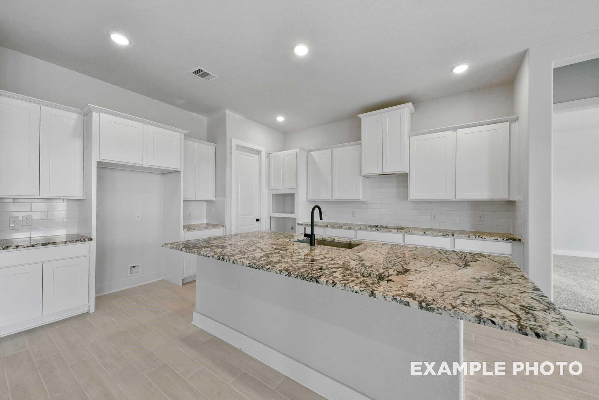 Modern open kitchen with white shaker cabinets, granite island countertop, and stainless sink in Davidson Homes The George A, Texas City
