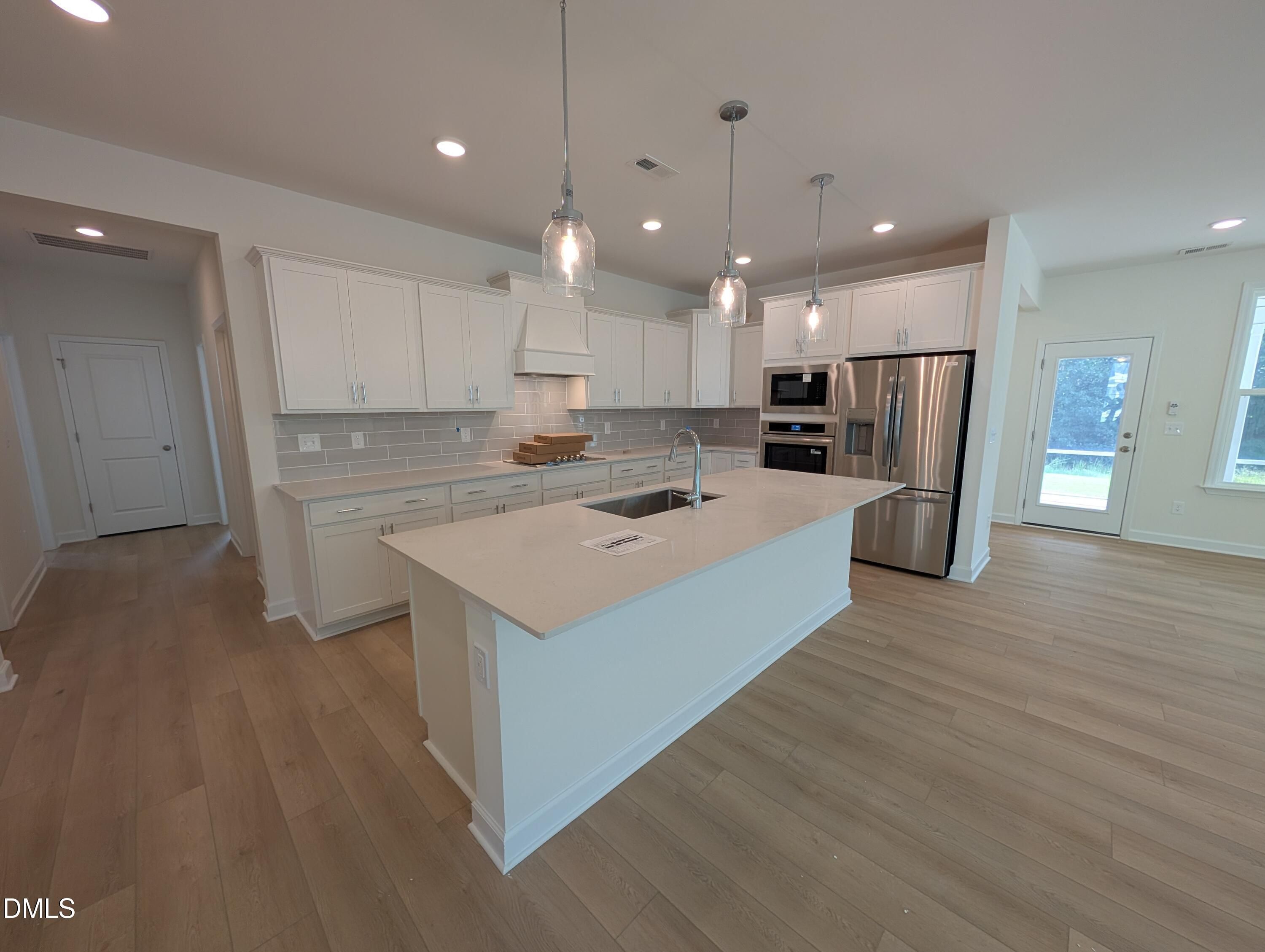 White kitchen with large island, pendant lights, and stainless appliances in Davidson Homes Magnolia A, Wendell Ridge, NC
