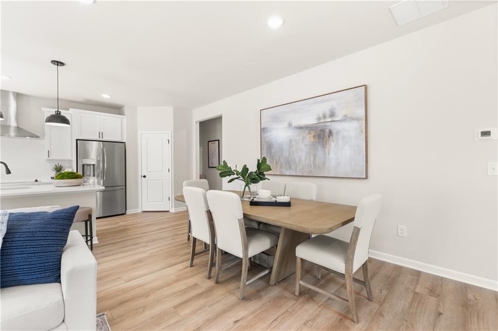 Modern dining room with wood table, white chairs, abstract wall art, and open kitchen in Davidson Homes The Burton C, Canton, Georgia